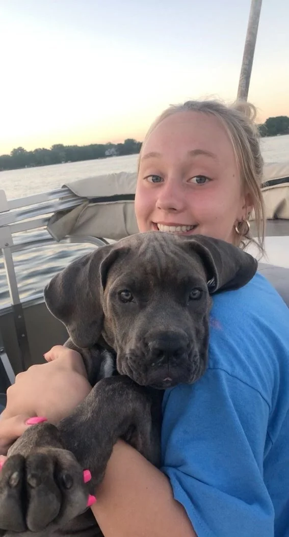 A girl holding a puppy on a boat during sunset with water and trees in the background.