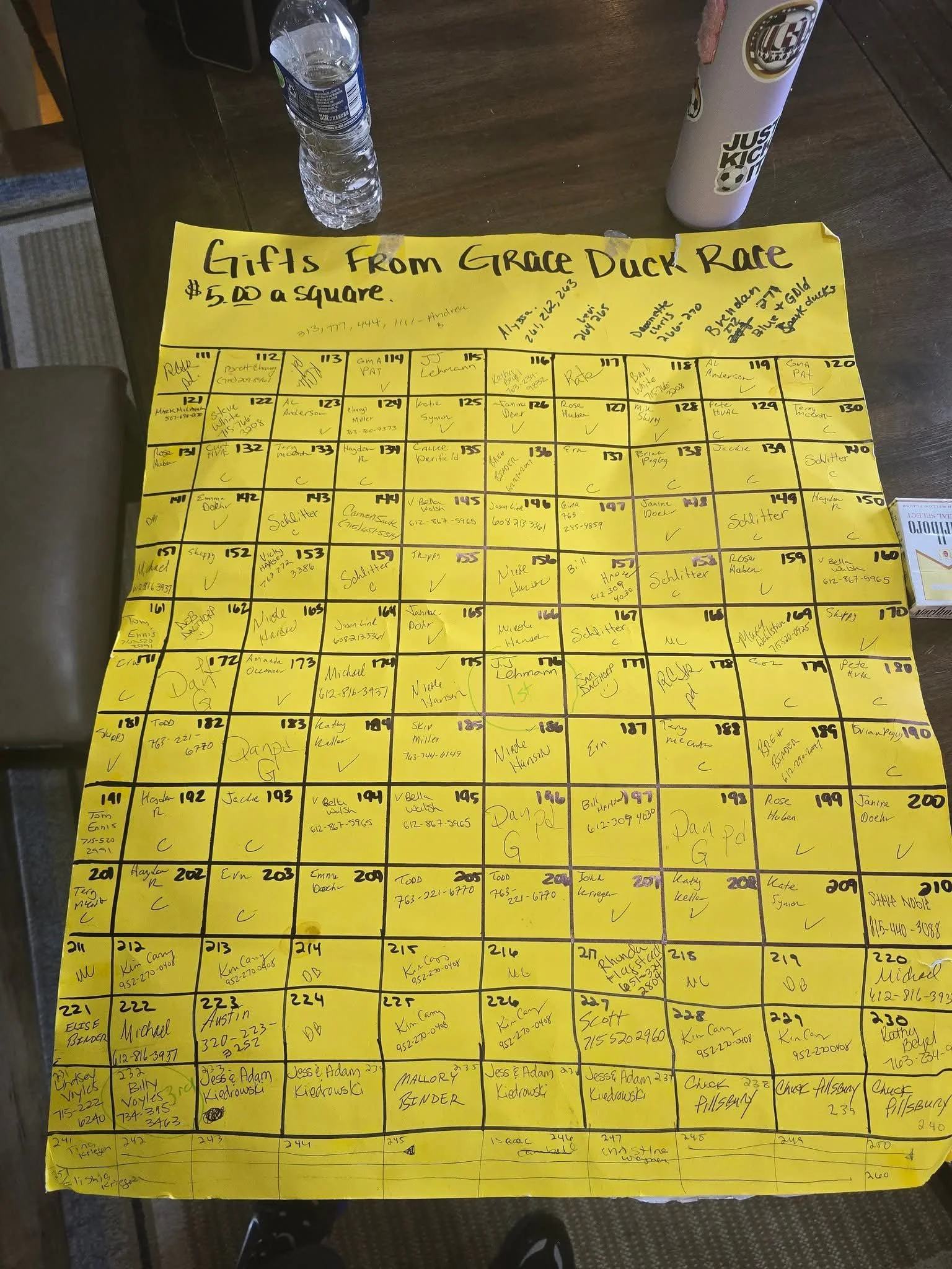 Yellow poster with handwritten sign labeled "Gifts from Grace Duck Race $5.00 a square," featuring a grid of numbered squares filled with names and contact info for a raffle or lottery.
