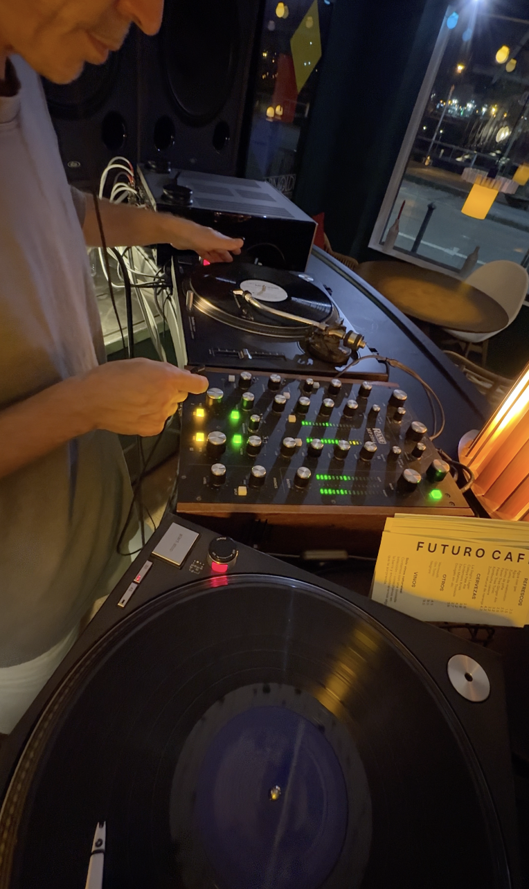 A DJ playing music with turntables and a mixer in a dimly lit café.