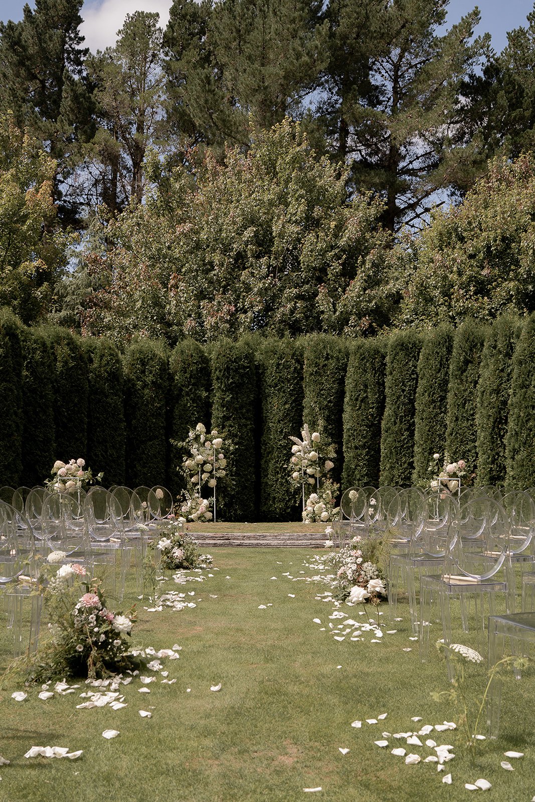 Outdoor wedding ceremony aisle with clear chairs and white floral arrangements.