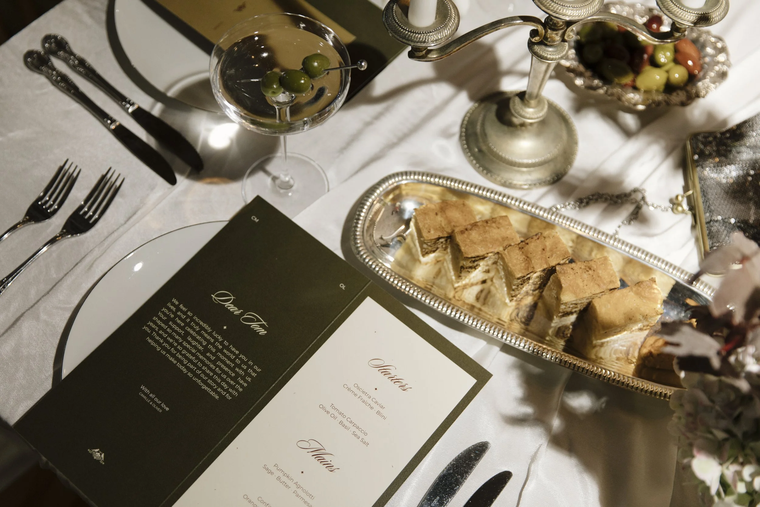 Custom wedding stationery with silver cutlery, glassware and canapés on a reception table.