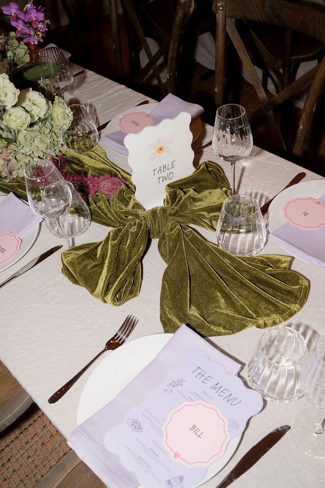 Wedding place settings with pink menus, green velvet napkins and crystal glasses.