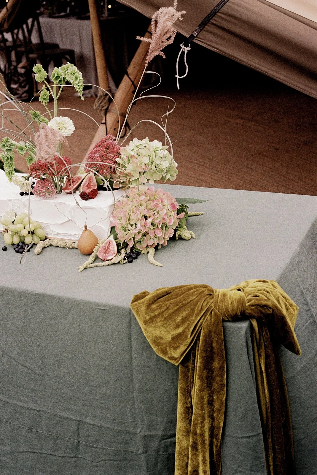 Green wedding table linen with a velvet bow, pastel flowers and trailing foliage.
