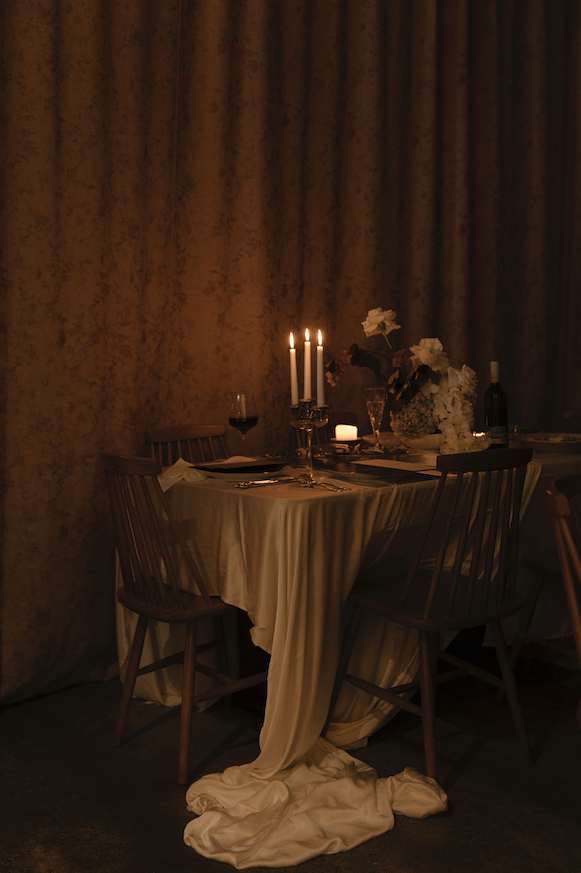 Candlelit wedding table with draped linen, flowers and wooden chairs.