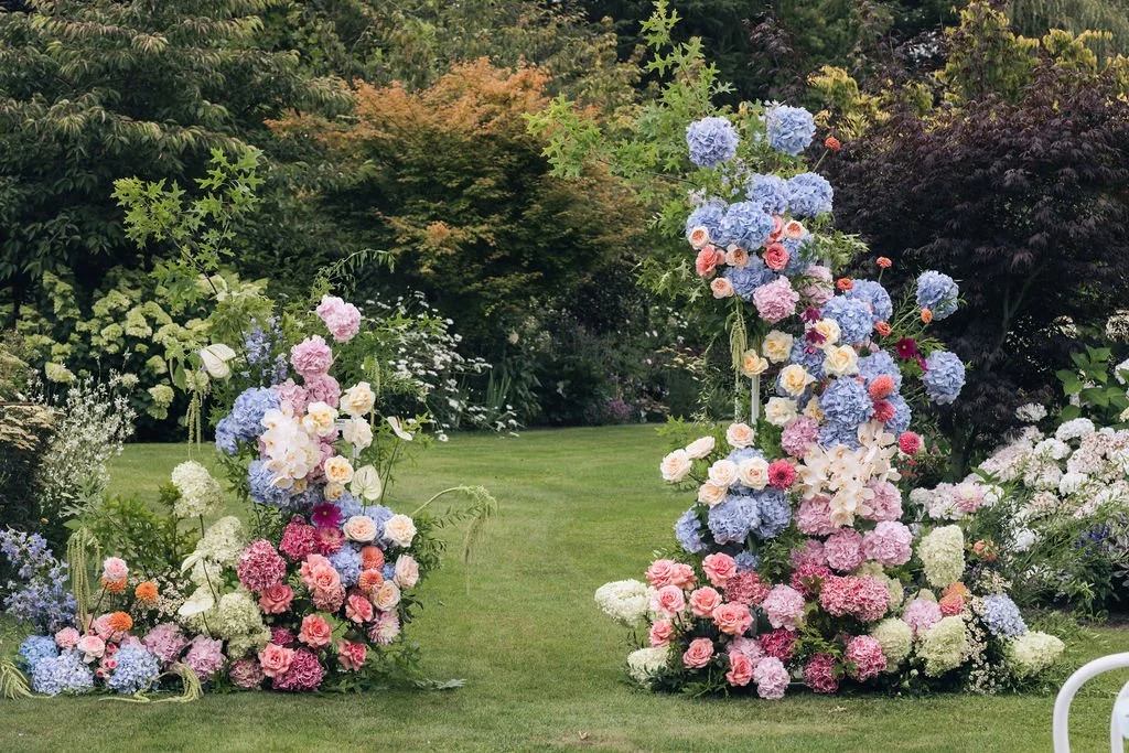 Colourful hydrangeas and roses arranged as a garden wedding ceremony backdrop.