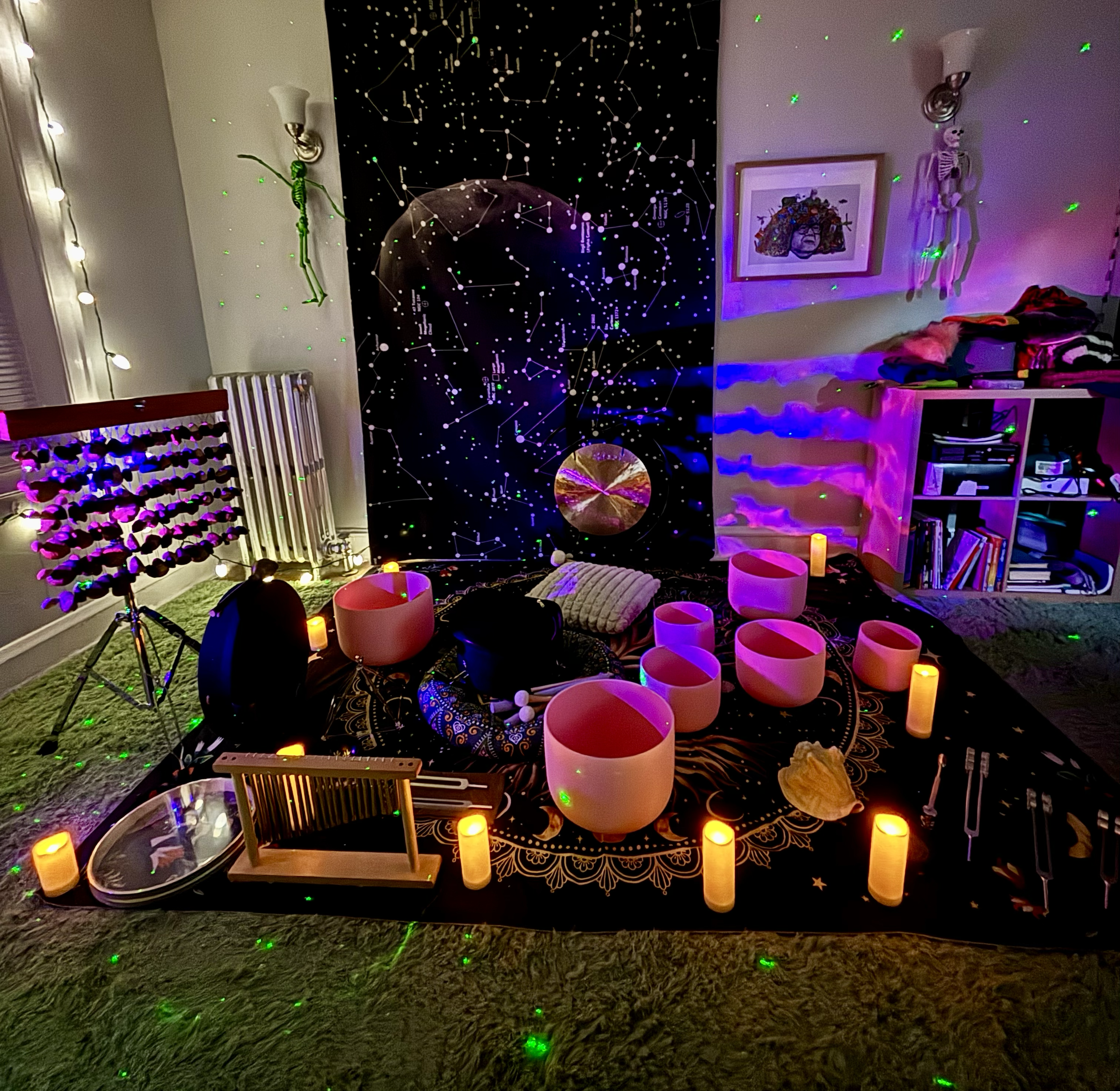 A cozy room setup with a large black star and constellation tapestry, crystal singing bowls, candles, a xylophone, and a variety of musical instruments, creating a calming and mystical atmosphere decorated with string lights and art on the walls.
