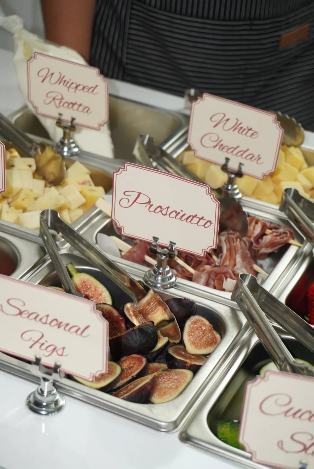 Selection of cheeses, cured meats, figs, and other toppings at a buffet.