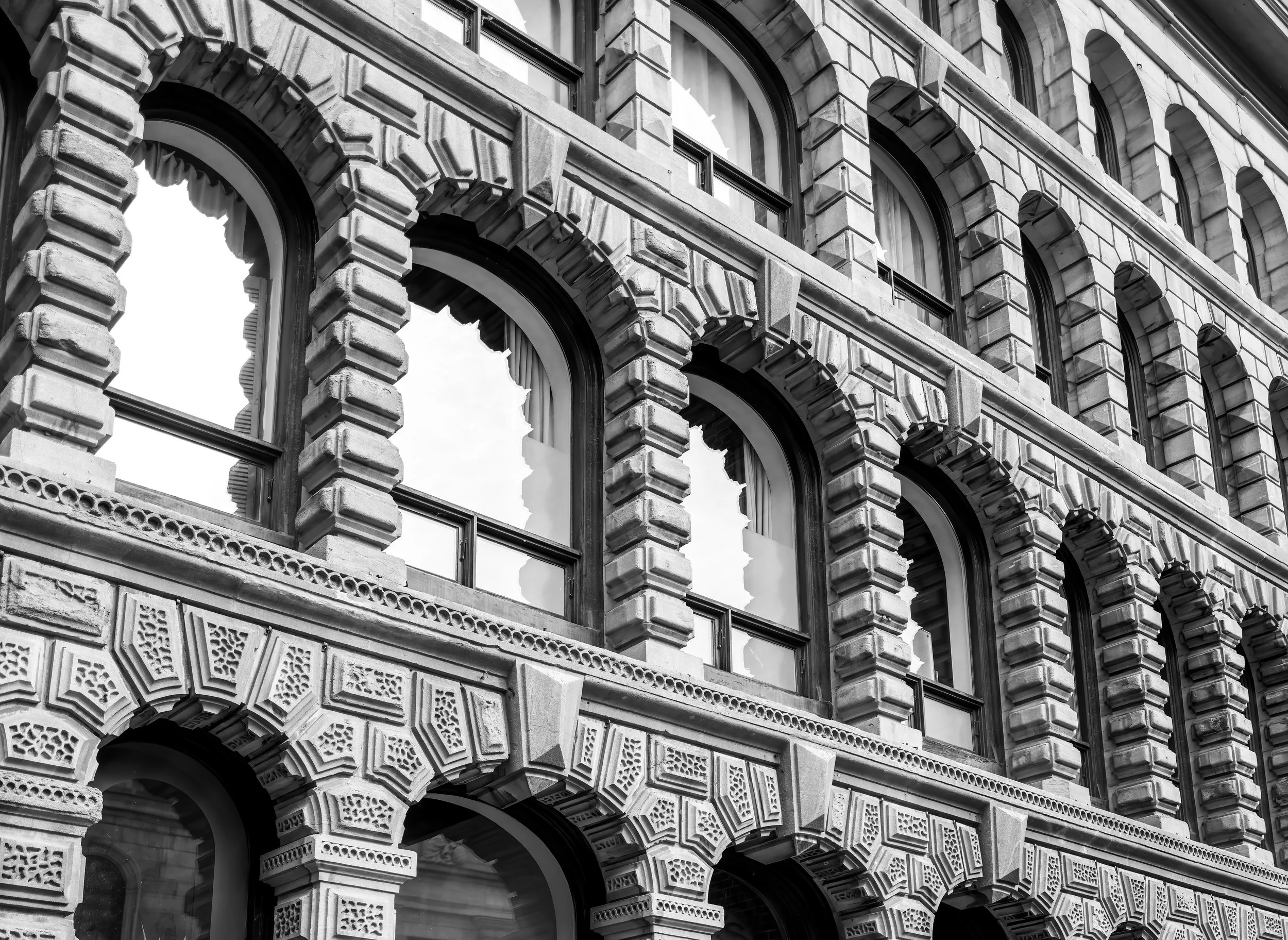 Close-up of a historic building's facade with ornate stonework, arched windows, and decorative patterns in black and white.