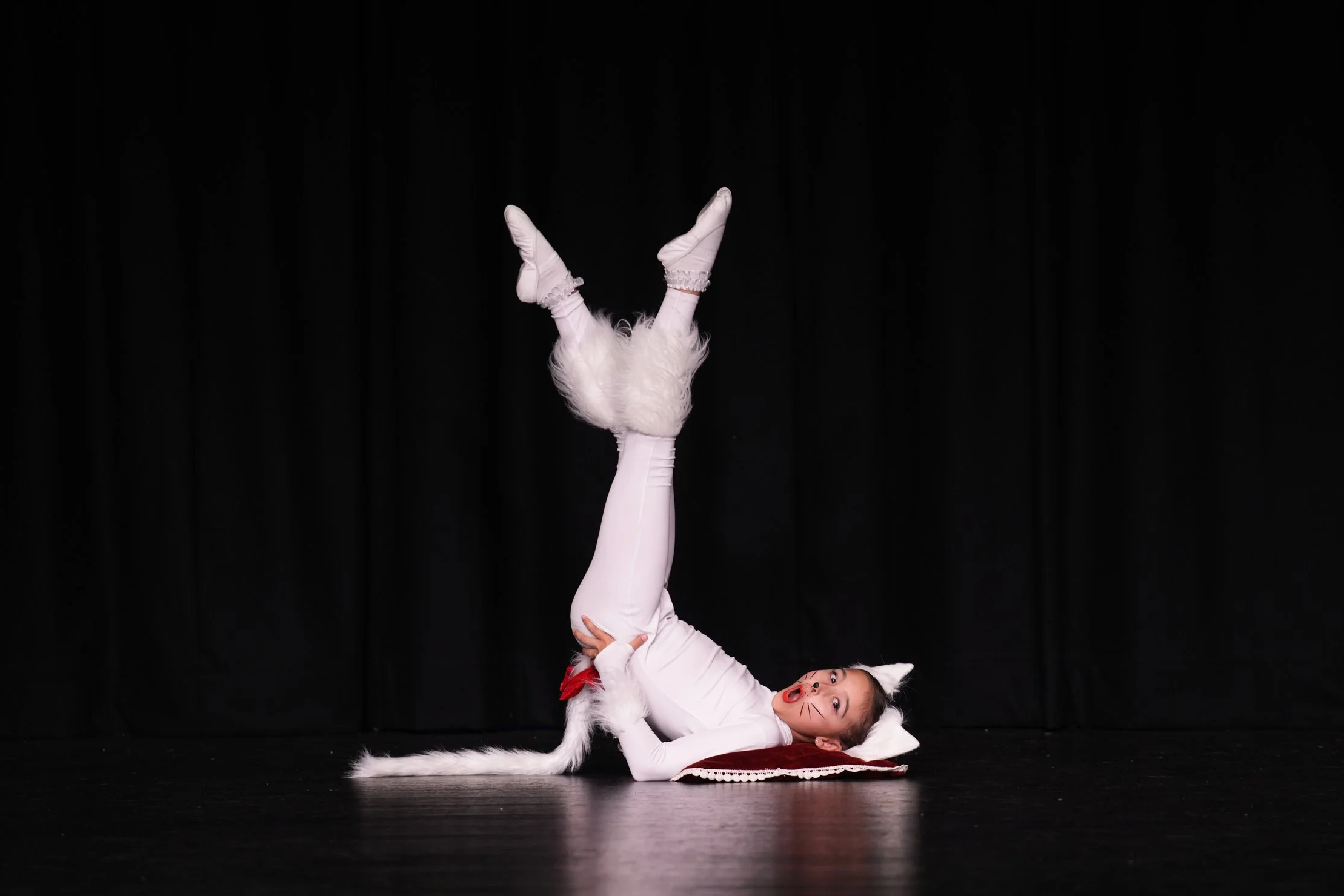Starbound performer dressed as a white cat lying on stage with legs raised during a theatrical dance performance.