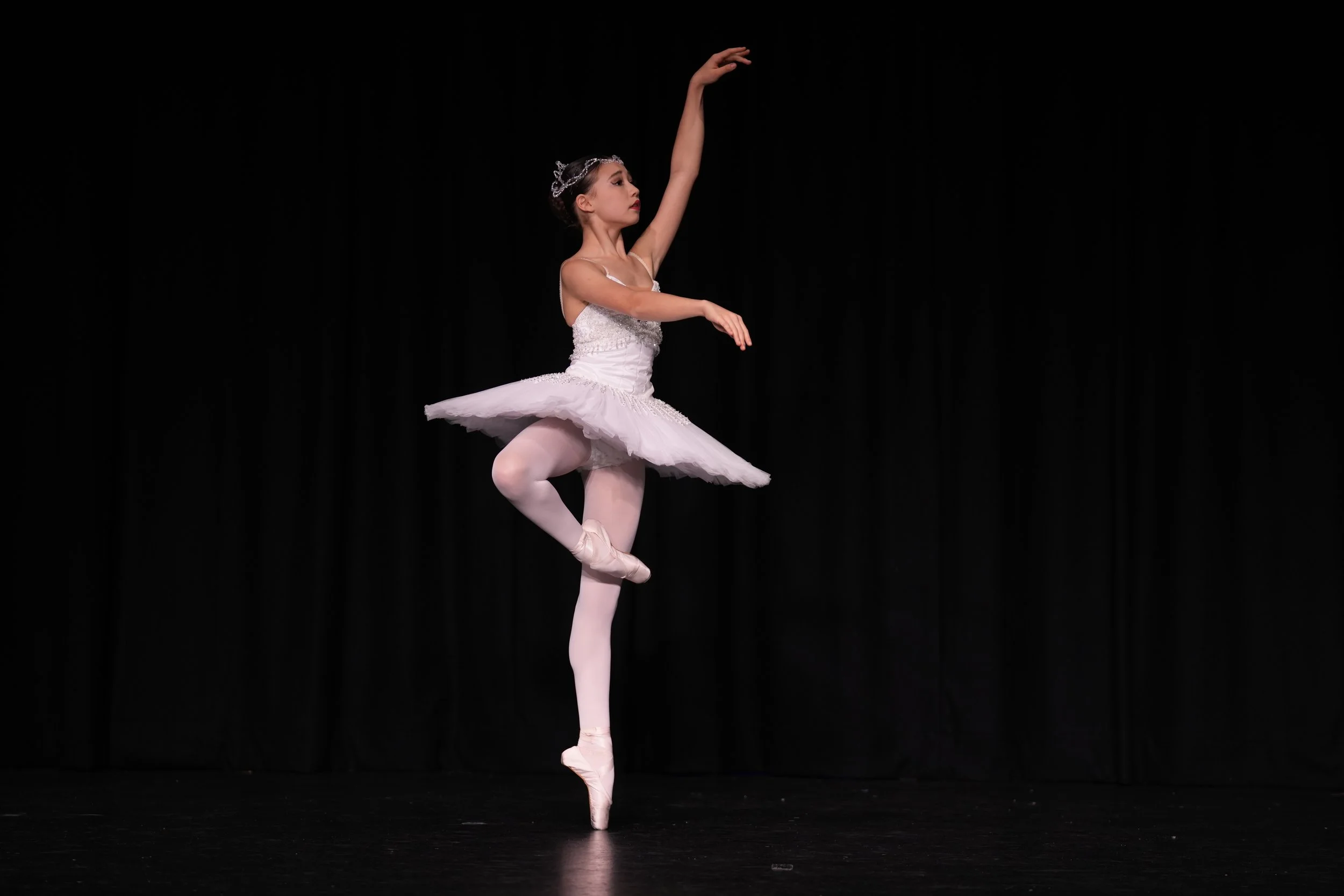 Starbound ballet dancer performing in a white tutu on stage with black background.