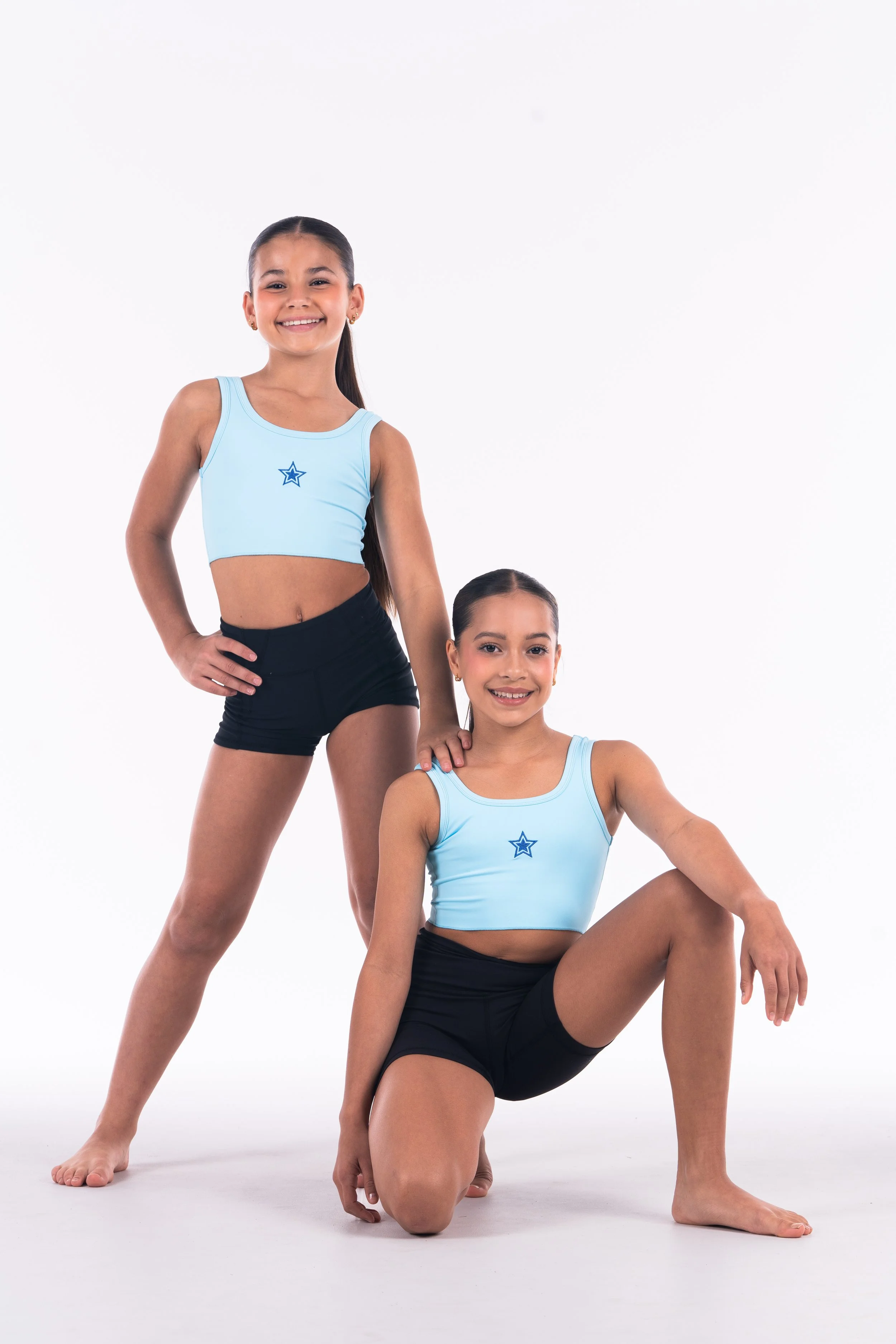 Two Starbound dancers in light blue crop tops with star logos and black shorts posing indoors against a white background.