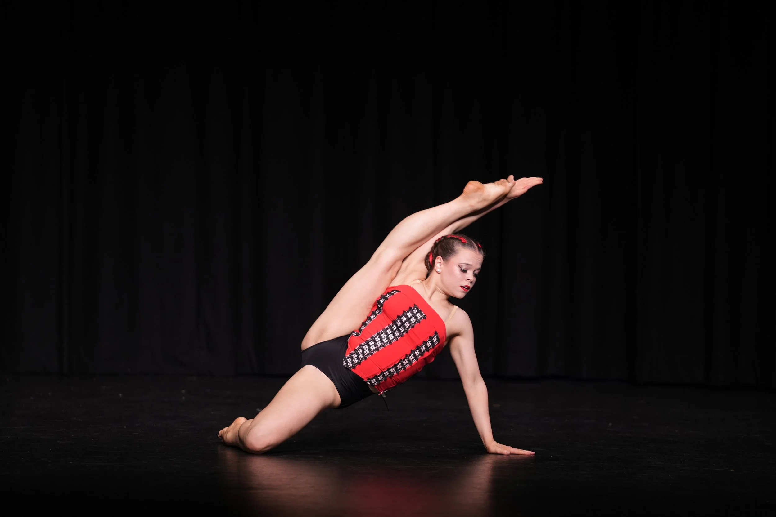 Female Starbound dancer performing on stage wearing red and black costume with black curtain backdrop.