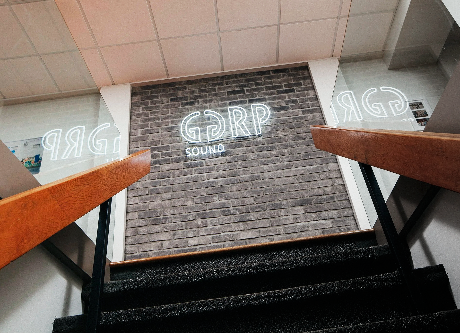 Neon sign reading 'GARR SOUND' on a brick wall, viewed from the bottom of carpeted stairs with wooden handrails.