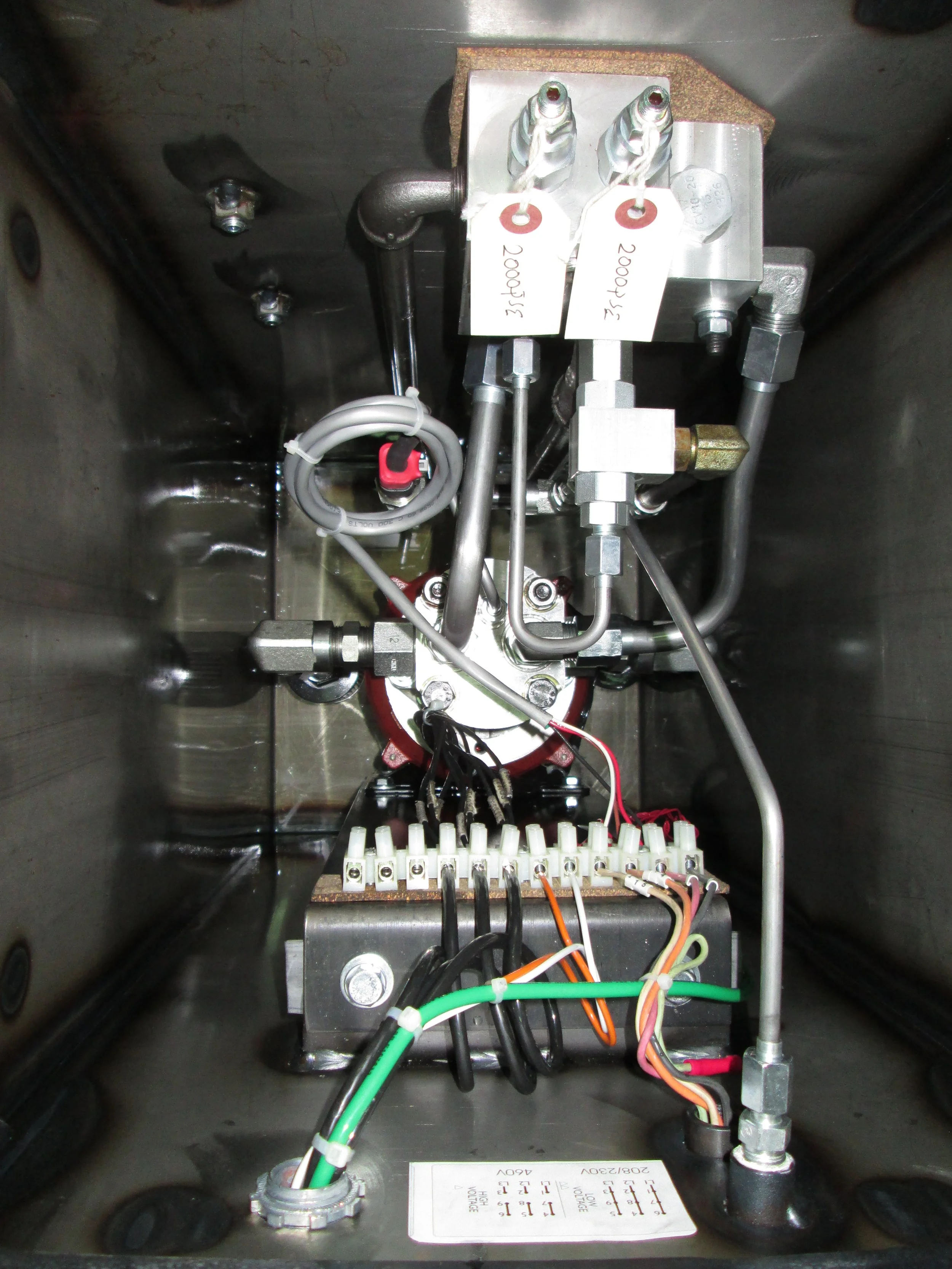 Electrical and hydraulic components inside an industrial control box, including wires, connectors, and metal fittings.
