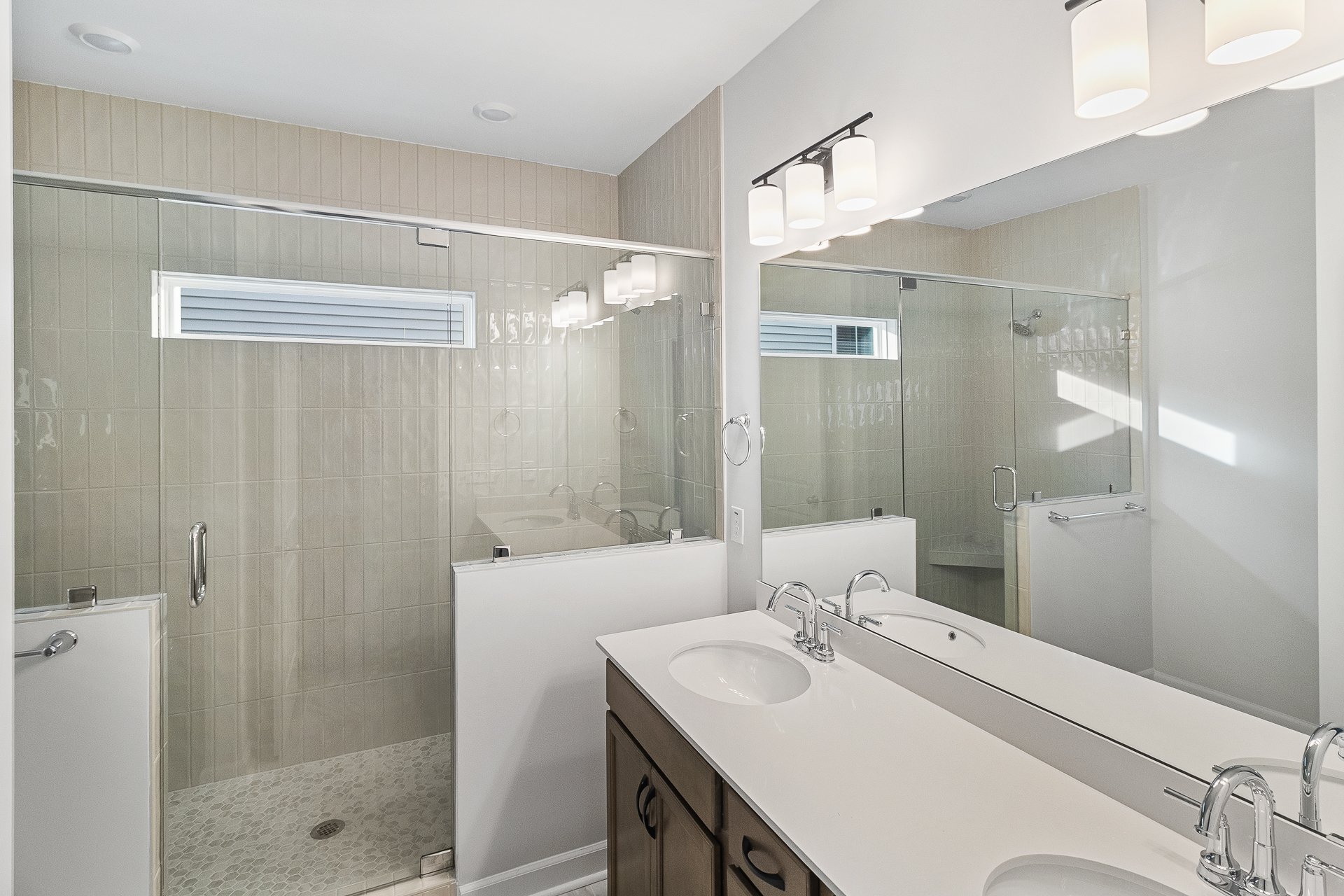 Bathroom with a double vanity mirror, sinks, and a glass-enclosed walk-in shower with tiled walls.