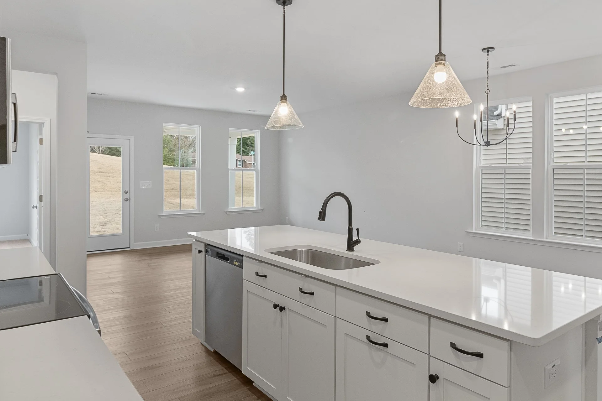Modern kitchen with white cabinets, a large island with a sink, black hardware, wood flooring, and natural light from multiple windows and a glass door.