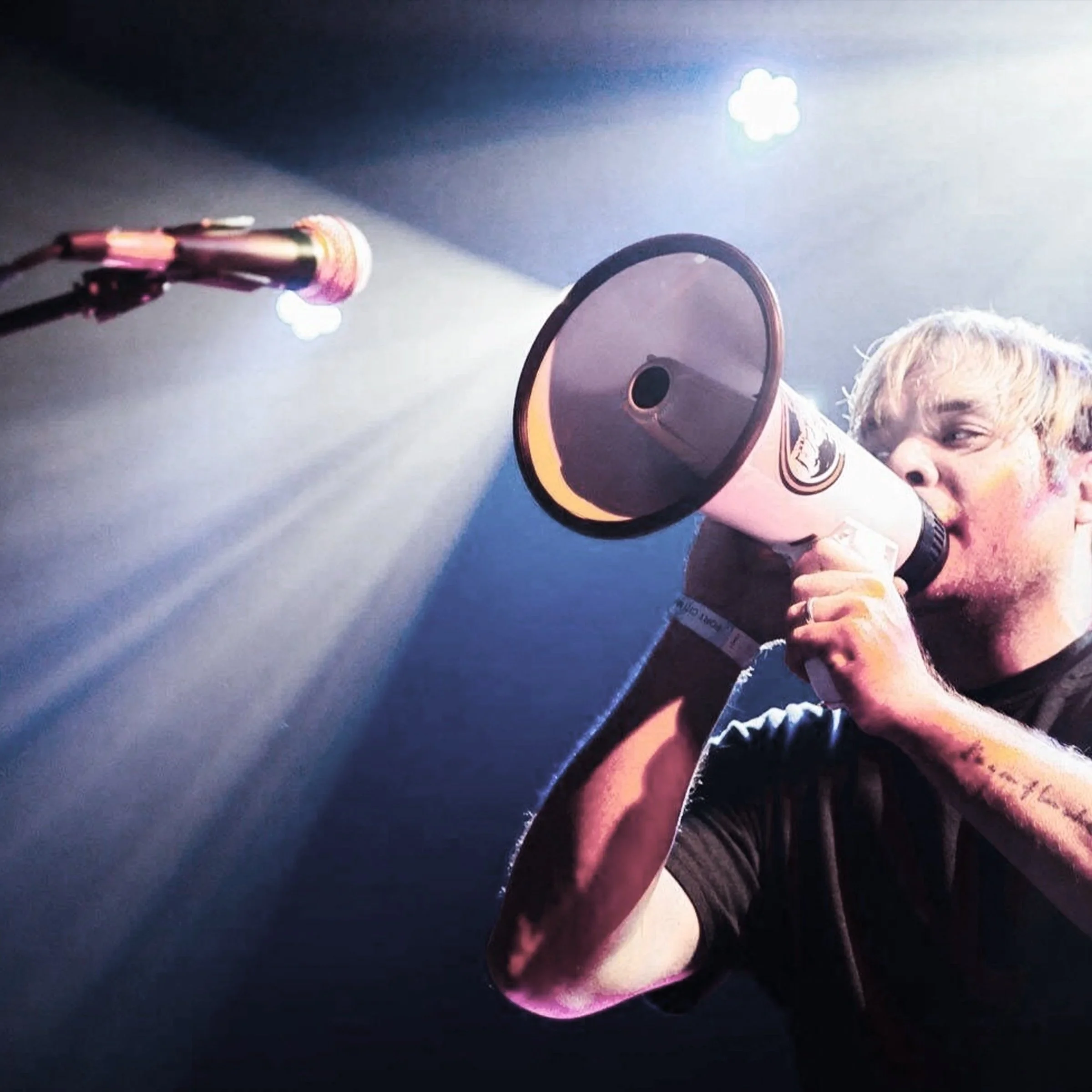 A person with white hair looking through a telescope with a black and gold exterior, projecting a bright light onto their face, against a dark background with some light sources.