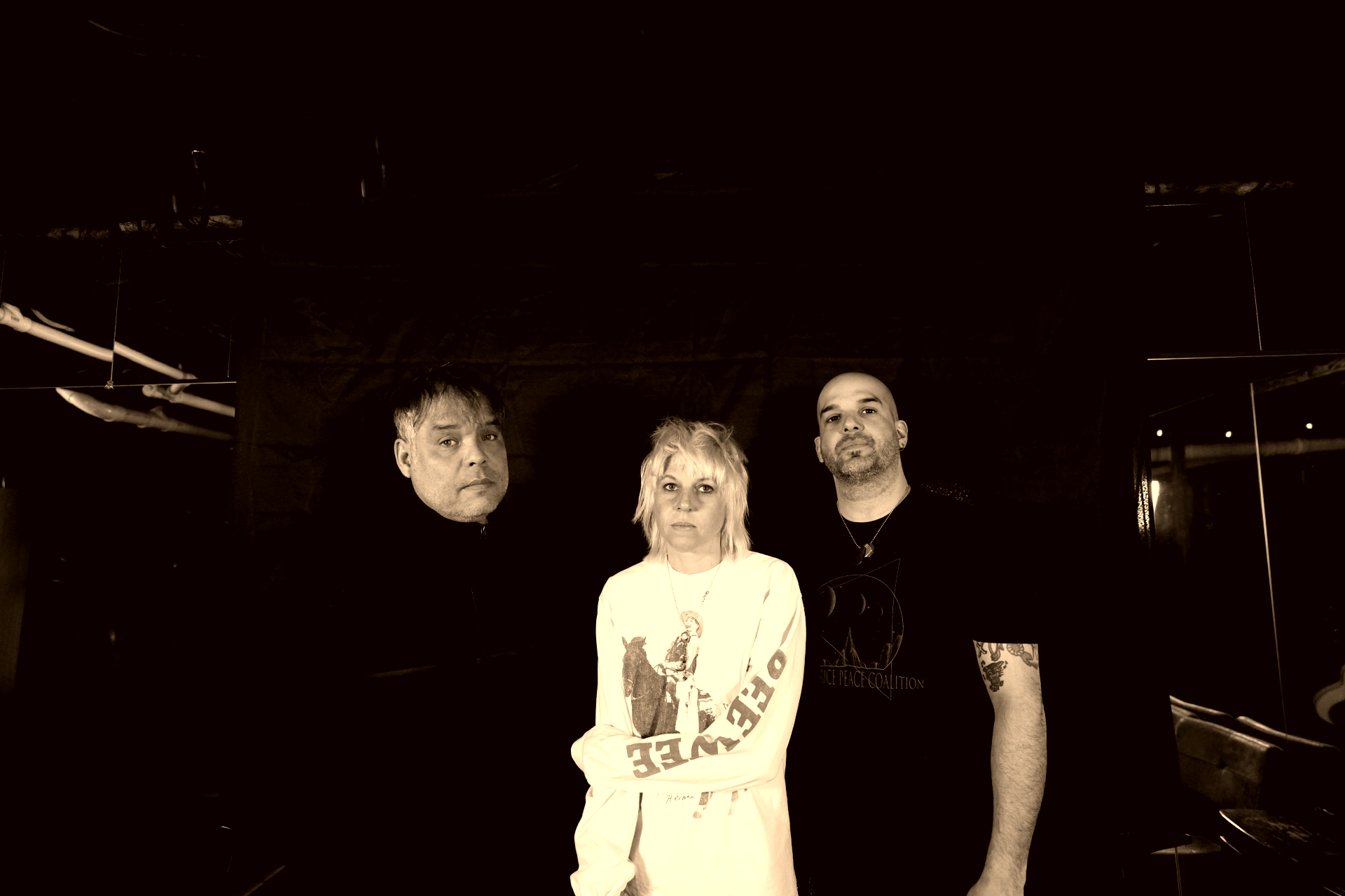 Four people standing together in a dimly lit room, with a dark background and mirrors reflecting light.