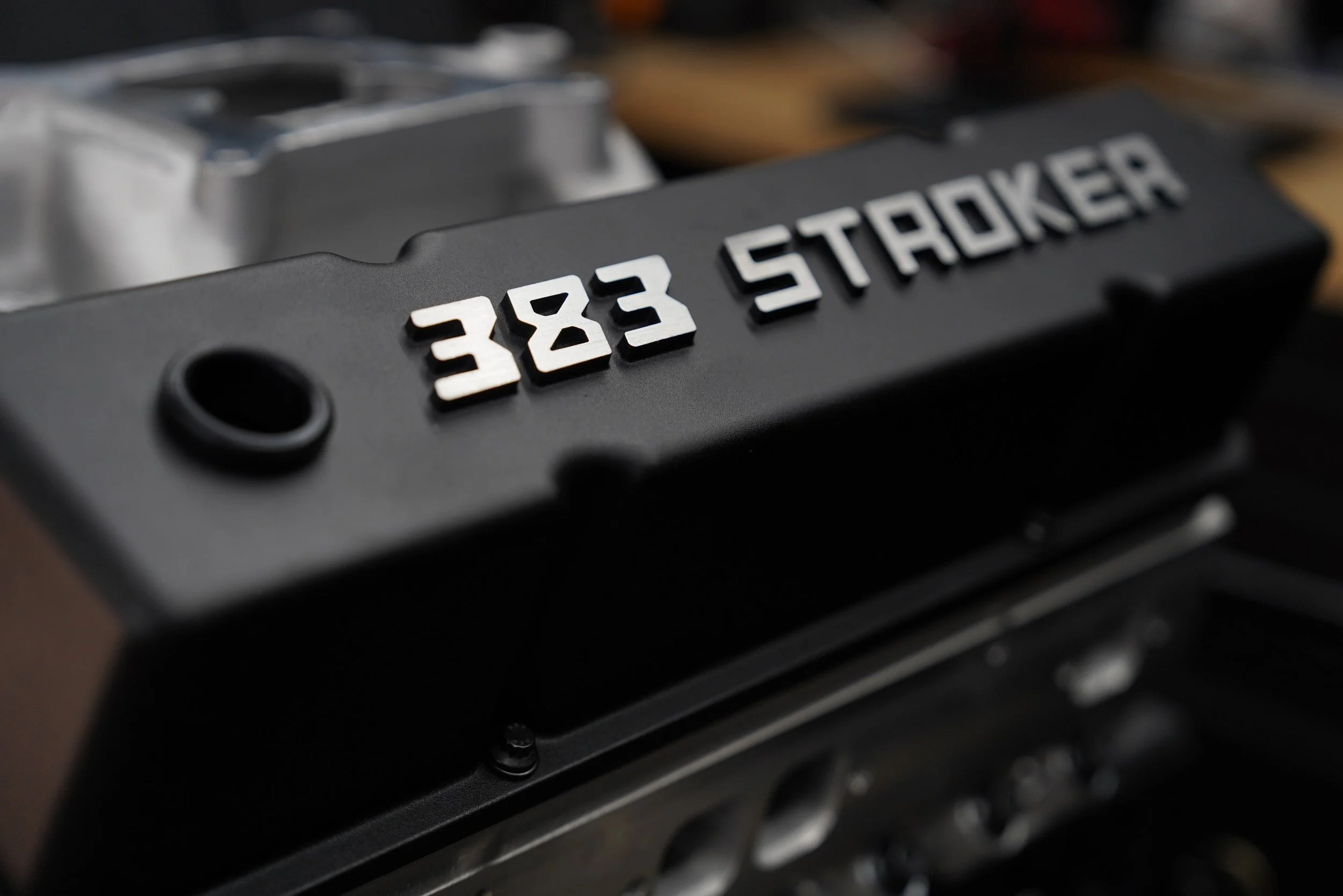 A close-up of a black badge with white 3D lettering reading '383 STOCKER' on a dark surface.