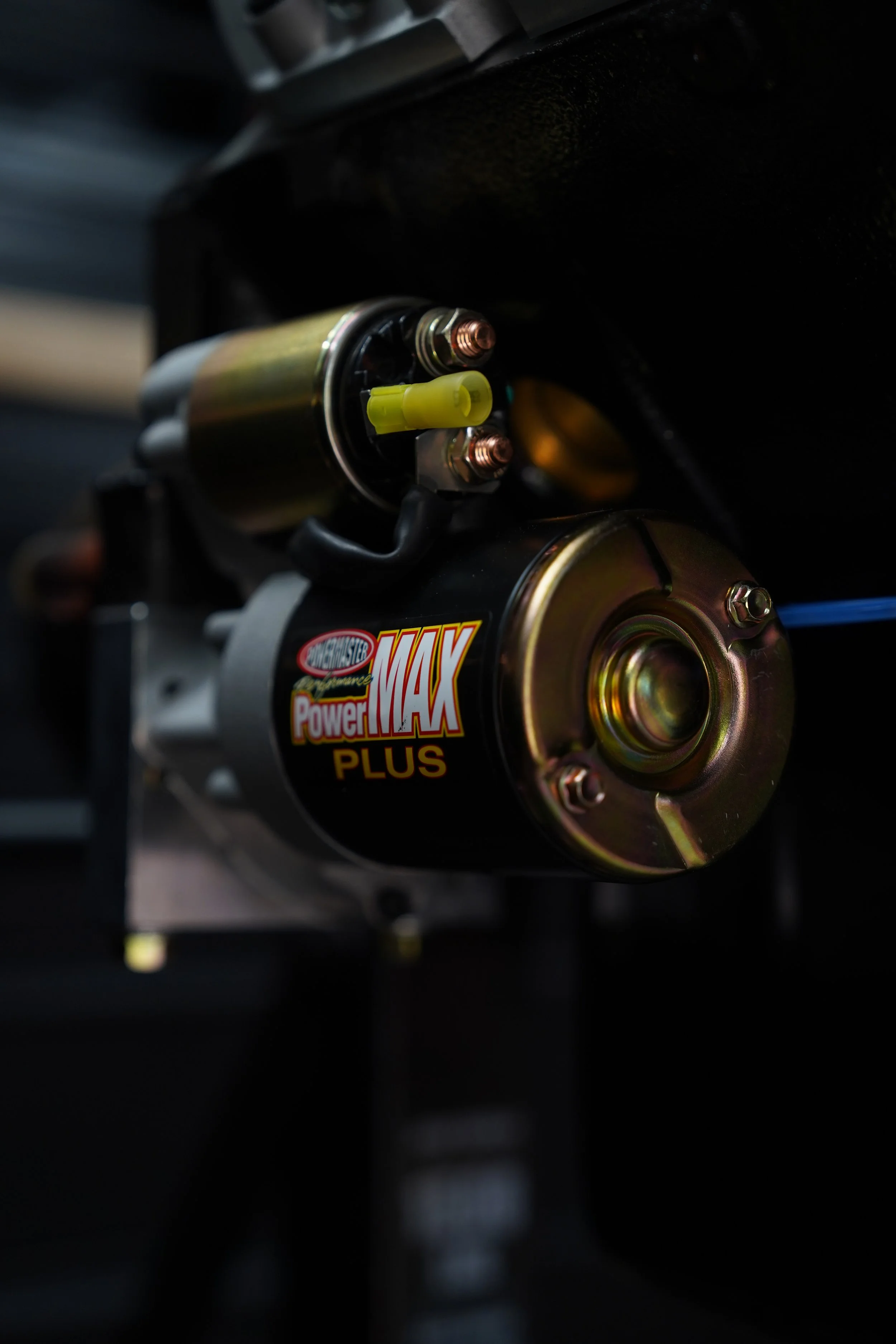 Close-up view of a small electric motor with a yellow connector, mounted on a black surface, with a sticker that reads 'Power MAX PLUS'.