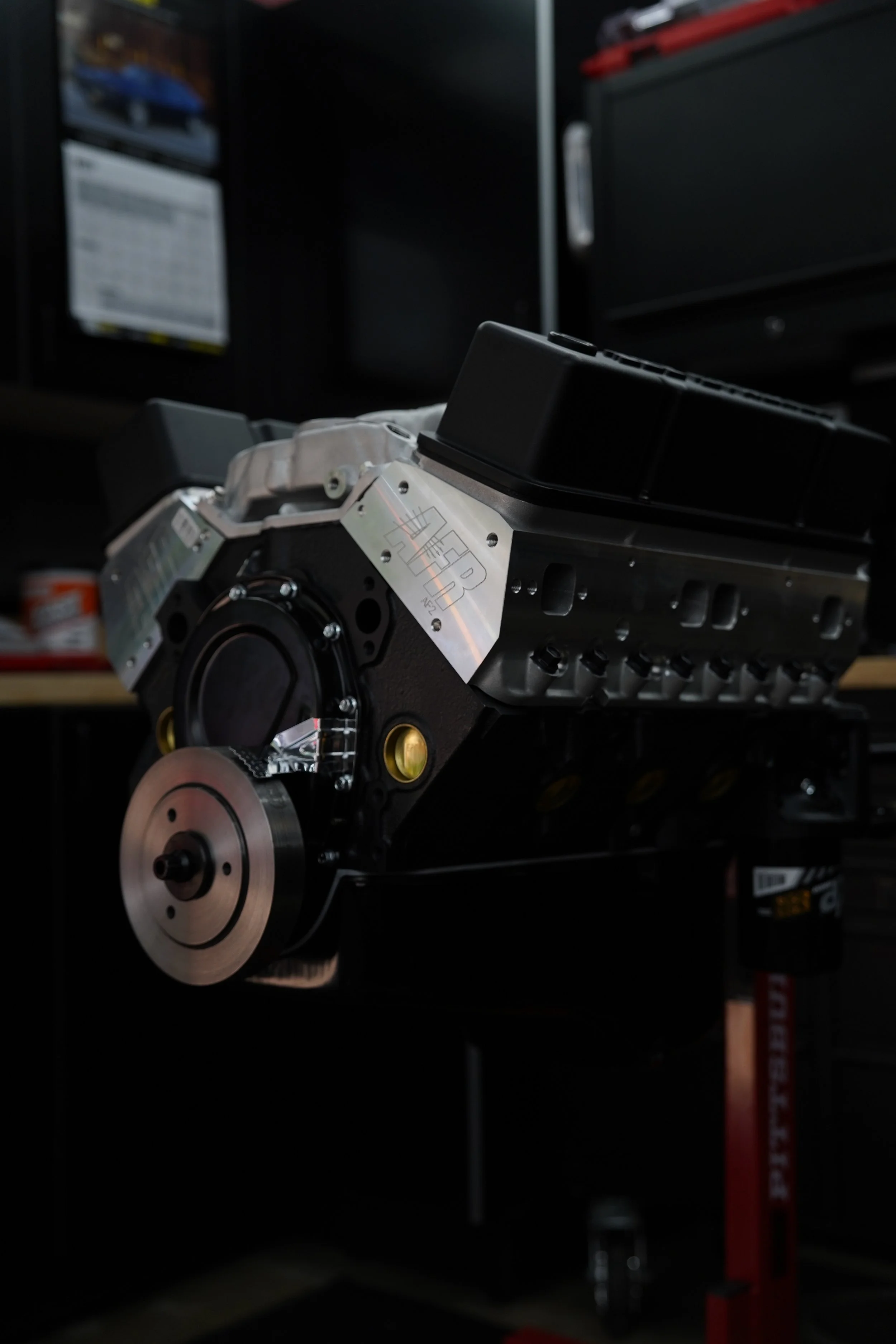 Close-up of a car engine or transmission component on a workbench in a garage, with tools and equipment in the background.
