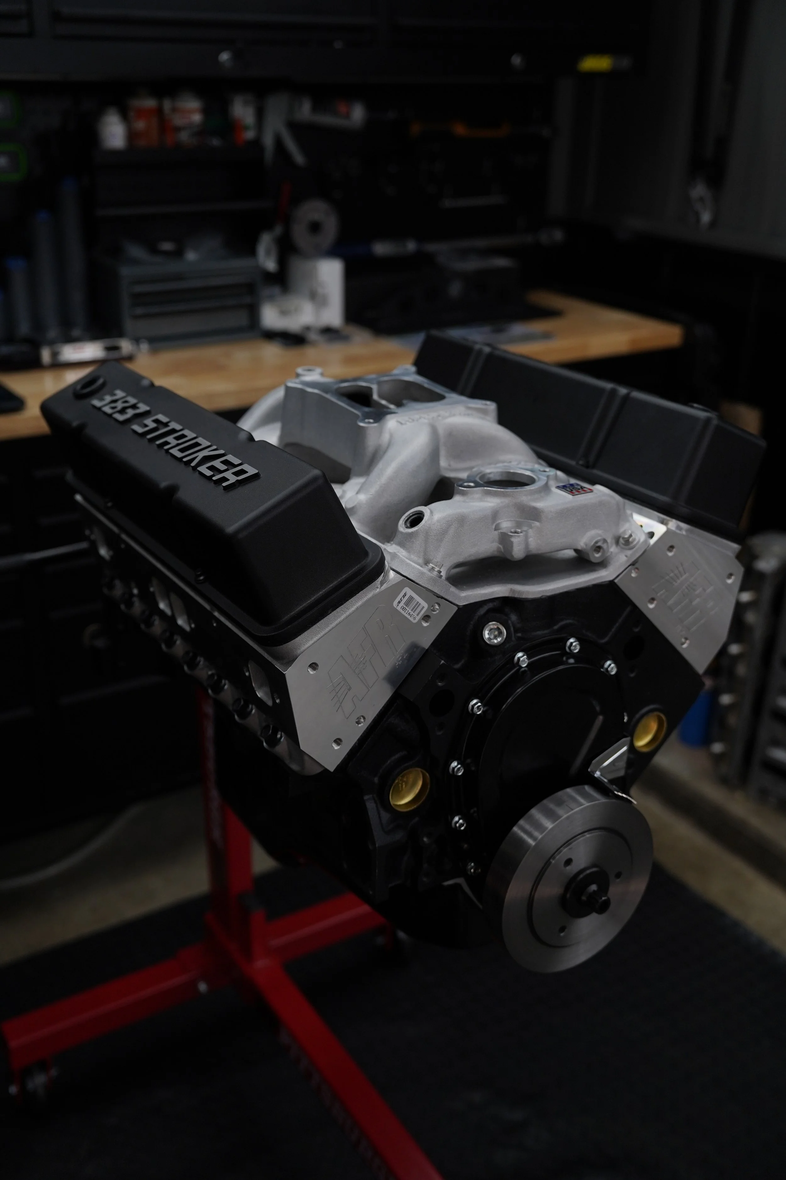 Close-up of a high-performance engine with parts labeled 'DPE SHOOTER' on a workbench in a garage or workshop.