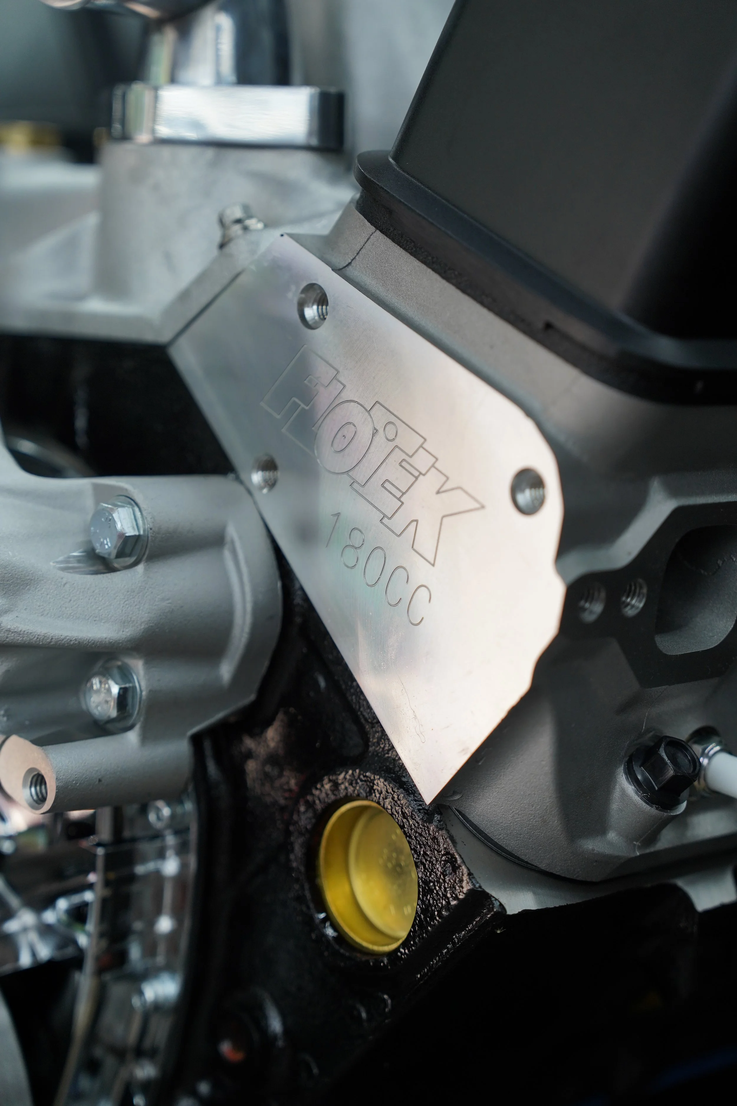 Close-up of mechanical engine components, including a metal plate with engraved text, bolts, and hoses, assembled in a complex configuration.