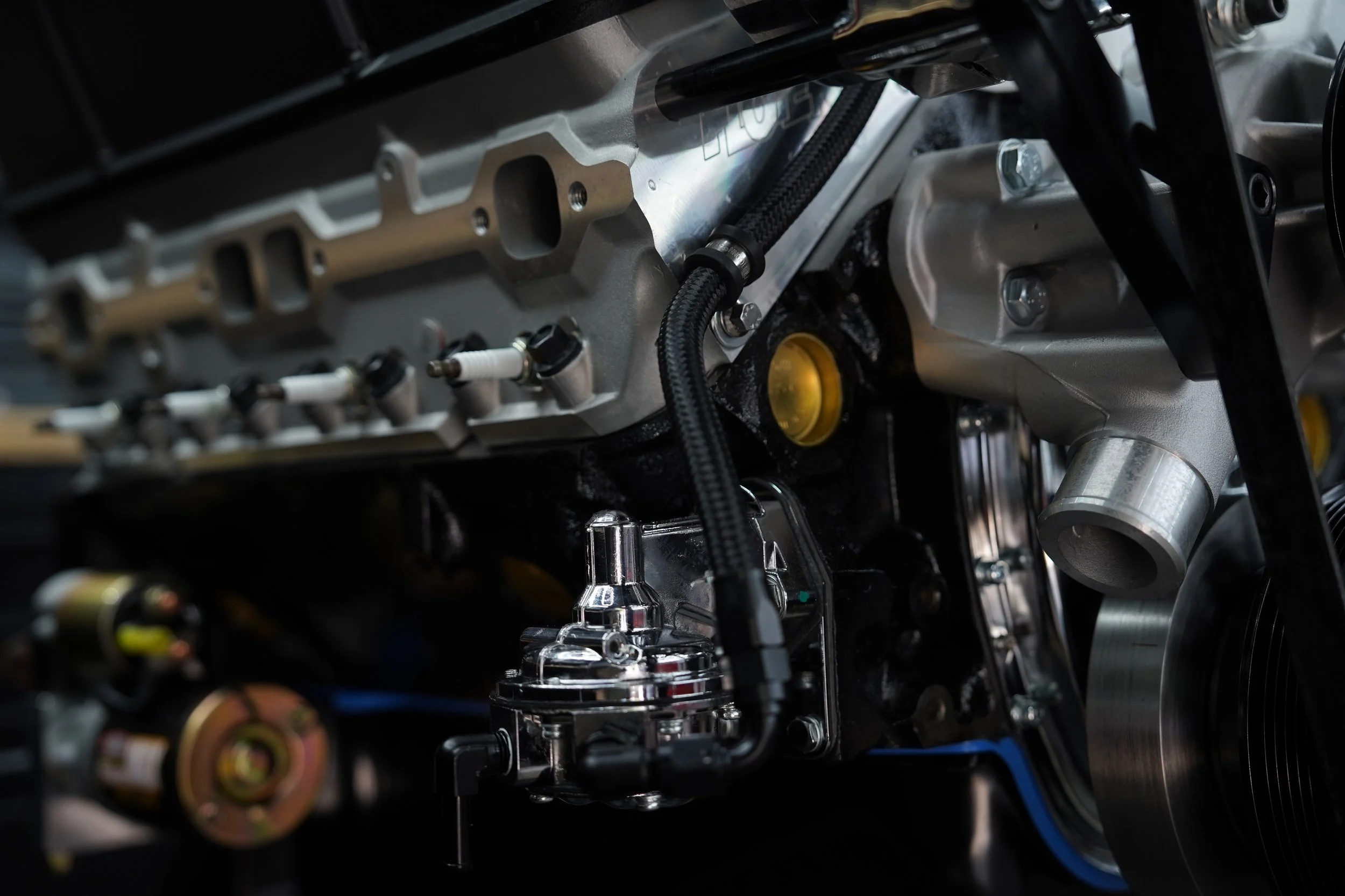 Close-up of an engine component with metallic parts, screws, and black hoses, likely part of a high-performance or racing engine.