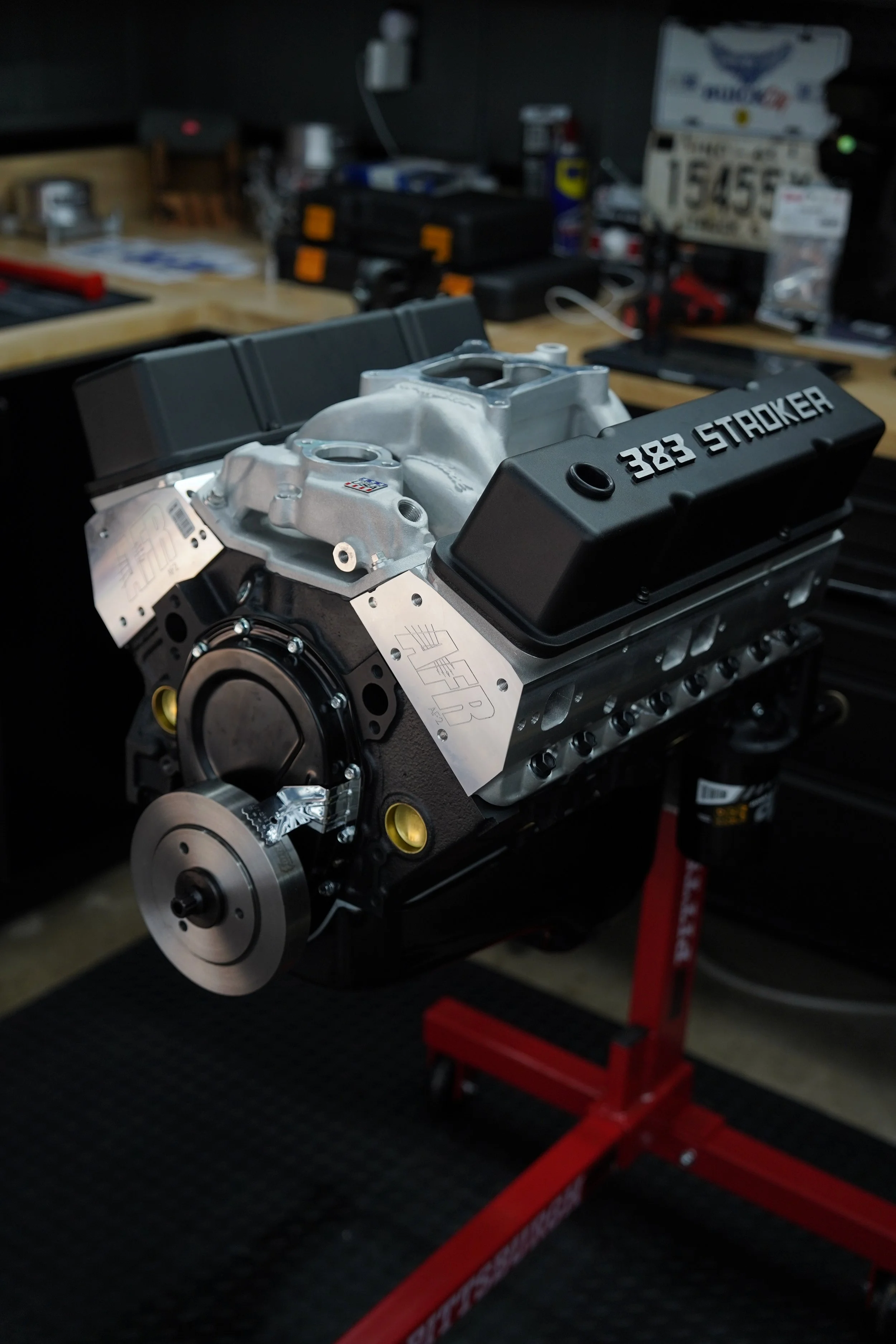 Close-up of a car engine on a workbench in a garage, with tools and equipment in the background.