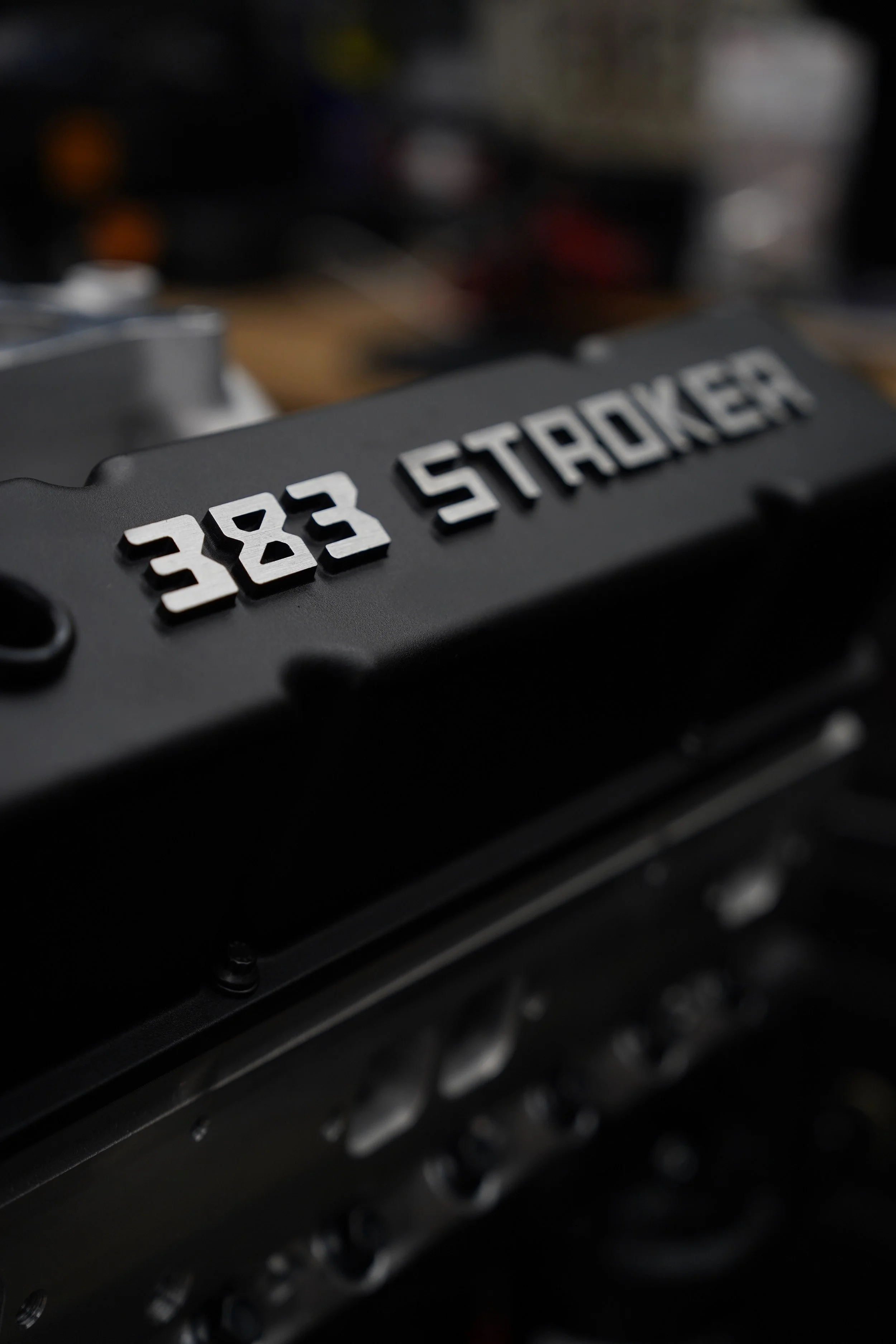 Close-up of a black object with white text reading '383 STACKER' and metallic details, blurred background.