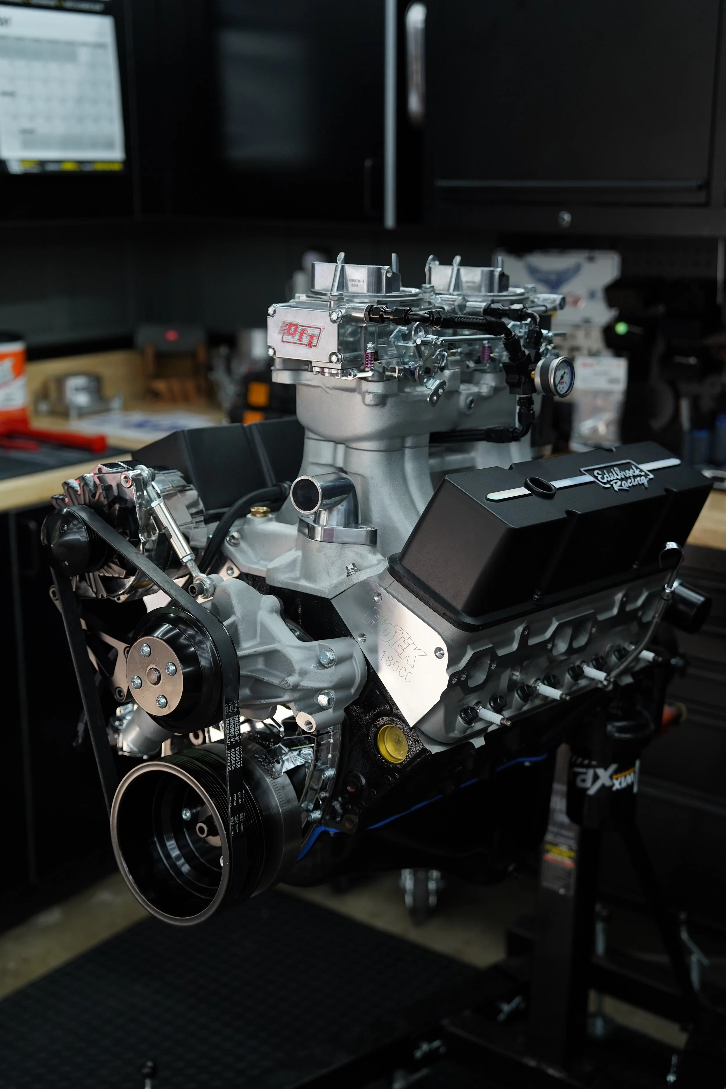 Close-up of a high-performance automotive engine mounted on a testing stand in a workshop, with various tools and equipment visible in the background.