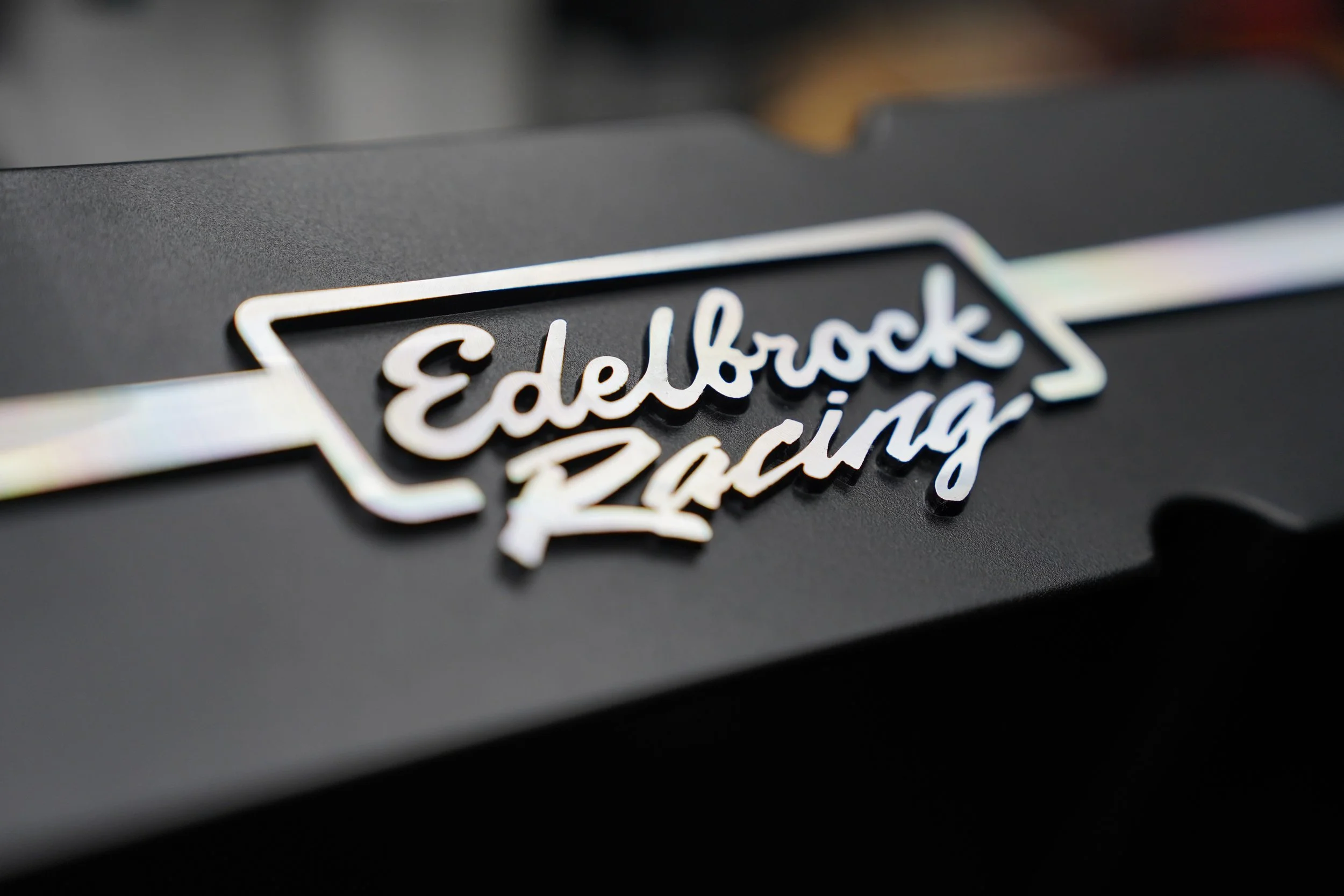 Close-up of a black electronic device with a metallic label reading 'Edelbrock Racing' in cursive script.