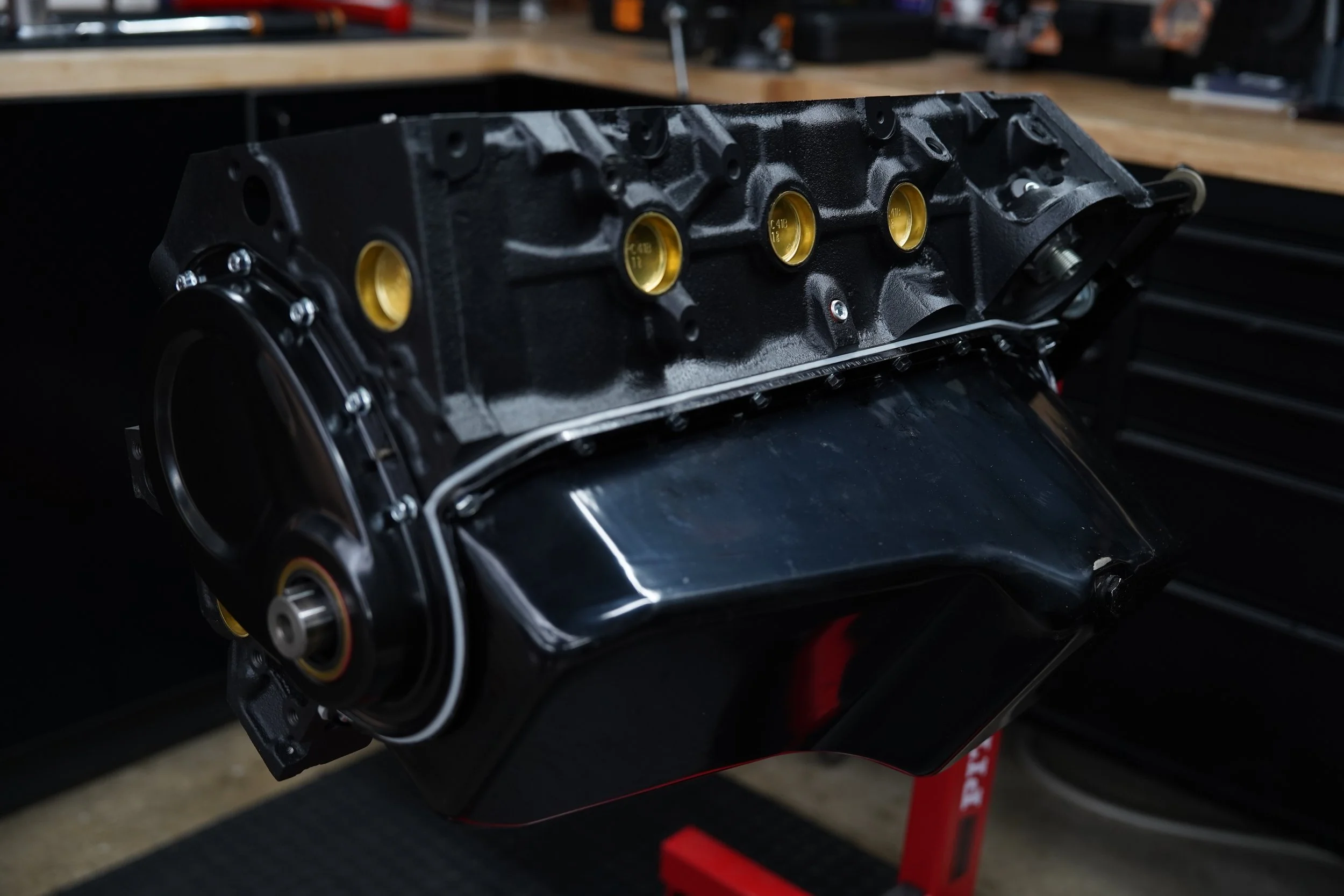 A black engine block with gold-colored cylinder sleeves on a workbench in a workshop.