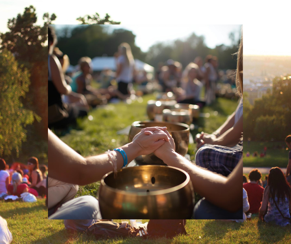 People sitting outdoors, holding hands, participating in a meditation or spiritual activity during a sunset event in a park.