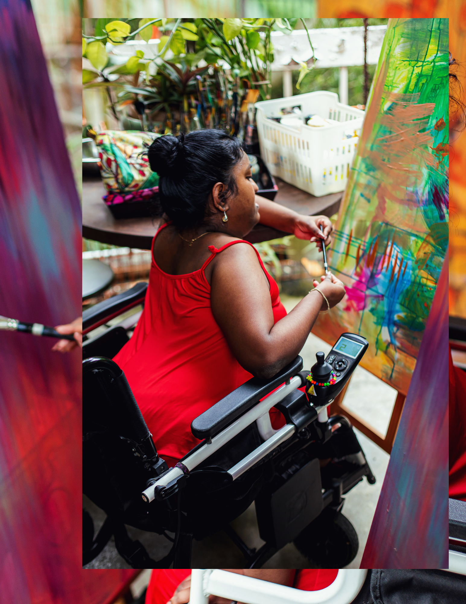 Woman in a wheelchair painting a colorful abstract on a canvas in an outdoor art studio.