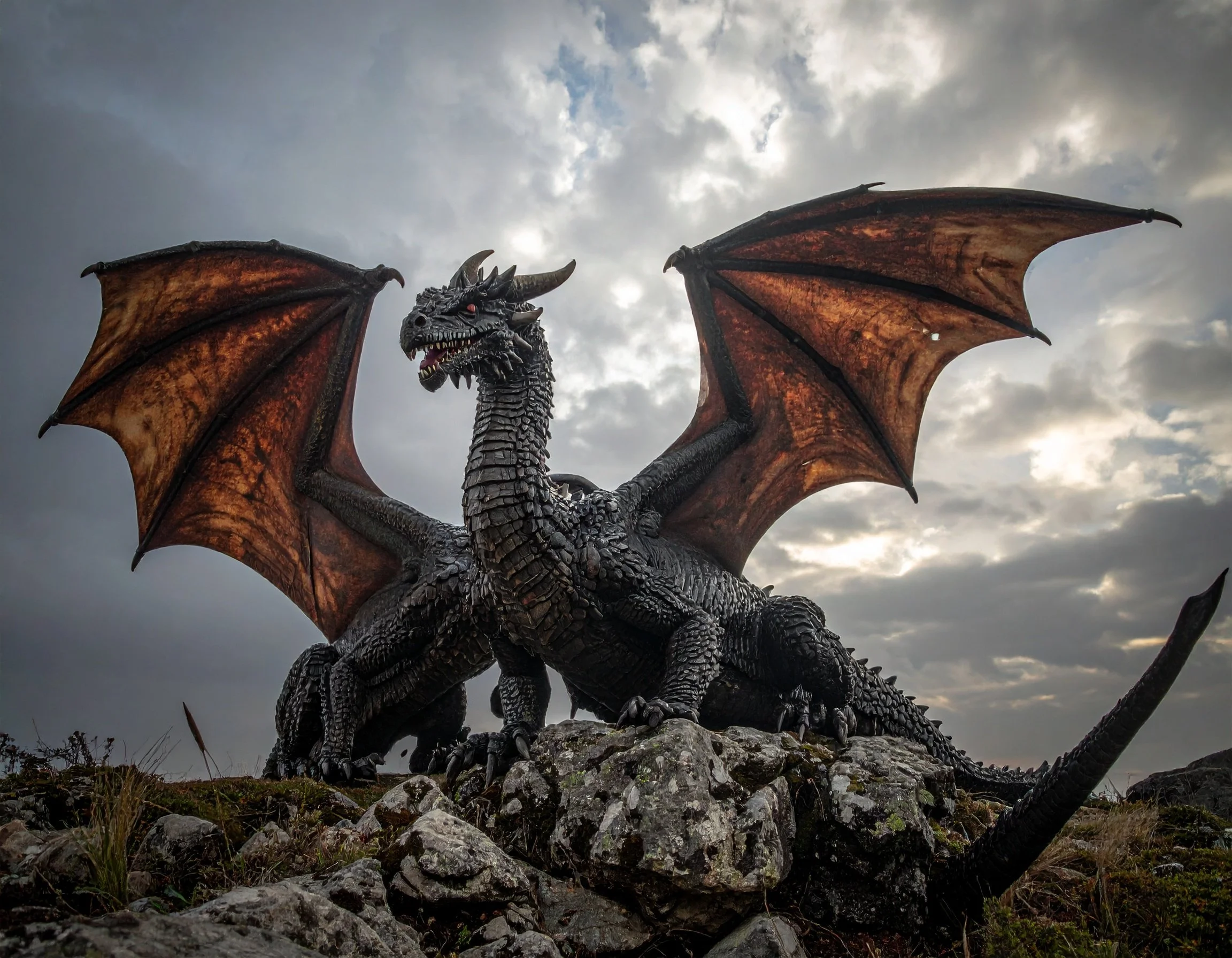 A detailed black and orange dragon statue with large wings and menacing expression, set against a cloudy sky