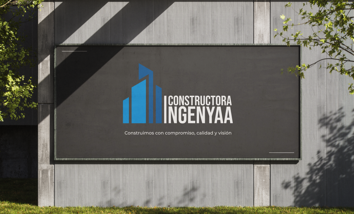 Valla publicitaria de INGENYAA sobre muro de concreto, con logotipo de barras ascendentes en color azul y el mensaje “Construimos con compromiso, calidad y visión”, rodeada de vegetación natural.