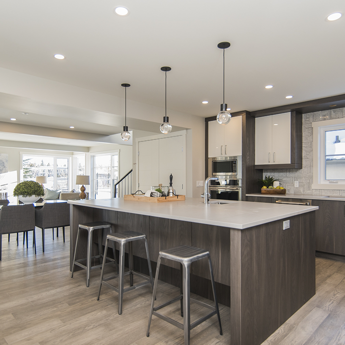 Cocina moderna de vivienda residencial con isla central, iluminación colgante y electrodomésticos de acero inoxidable, integrada a comedor y sala con amplios ventanales, proyecto de construcción habitacional.