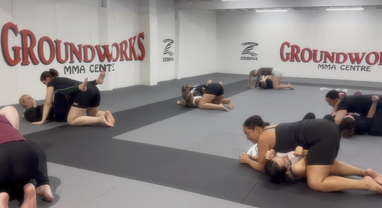 Multiple women practicing Brazilian Jiu-Jitsu grappling techniques on padded mats at Groundworks MMA Center.