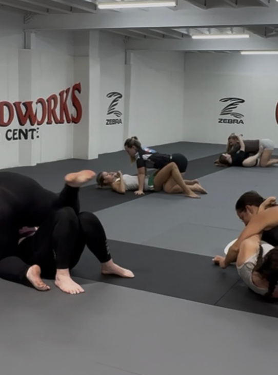 People practicing Brazilian jiu-jitsu on mats in a training gym.