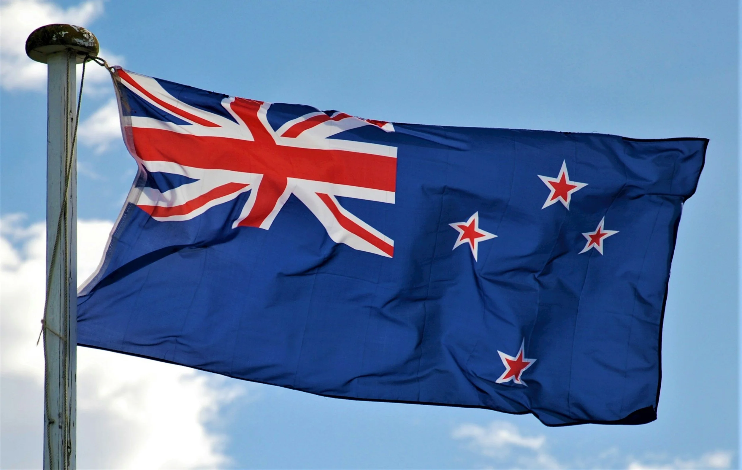 The New Zealand flag flying on a flagpole against a partly cloudy sky.