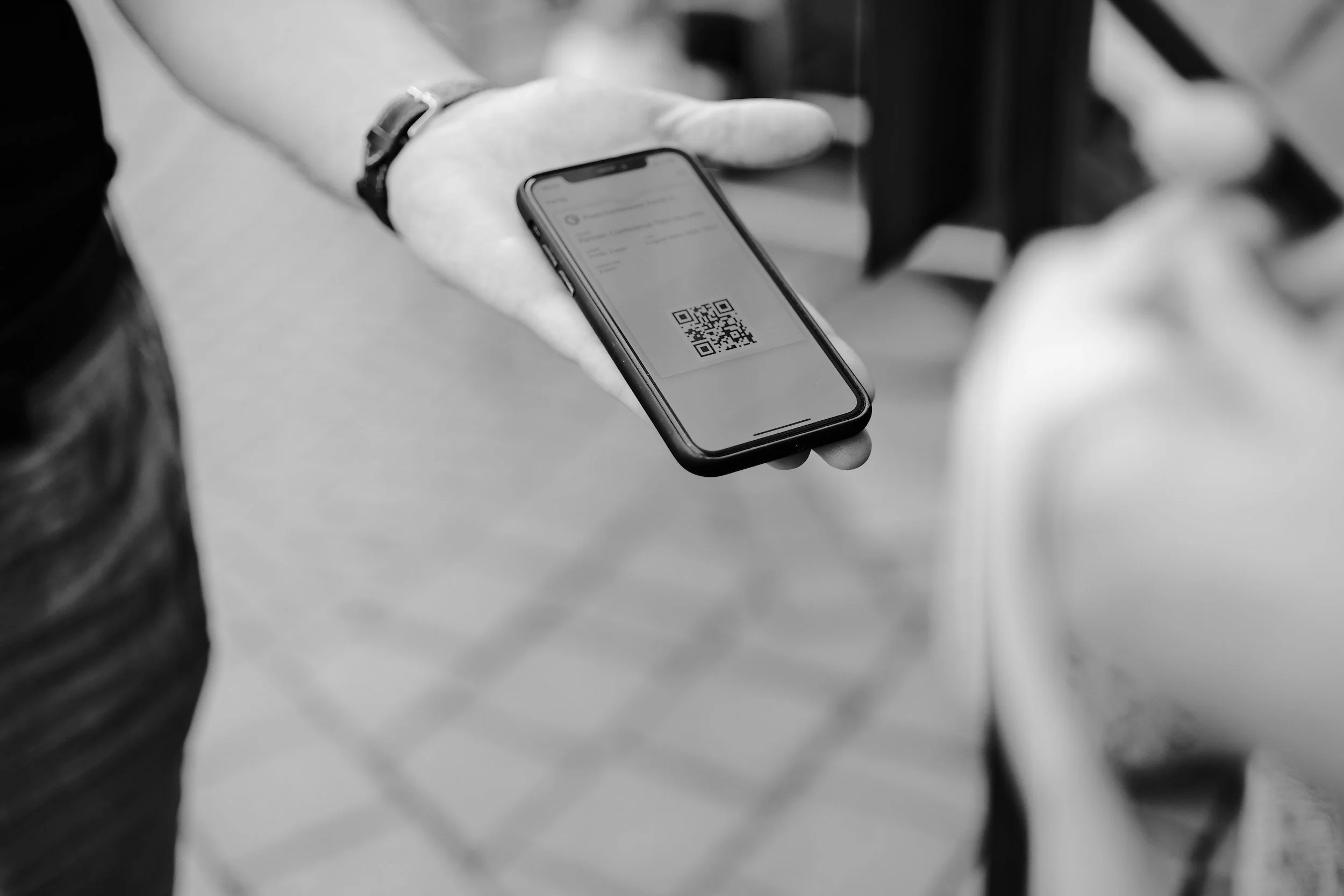 A person holding a smartphone displaying a QR code on the screen, in black and white.