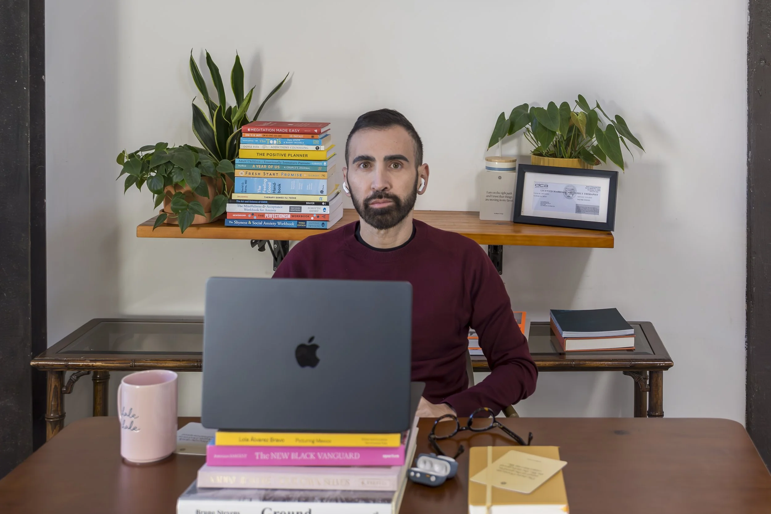 Alex Barragan, LGBTQ-affirming therapist in Los Angeles, smiling at his Westwood office desk