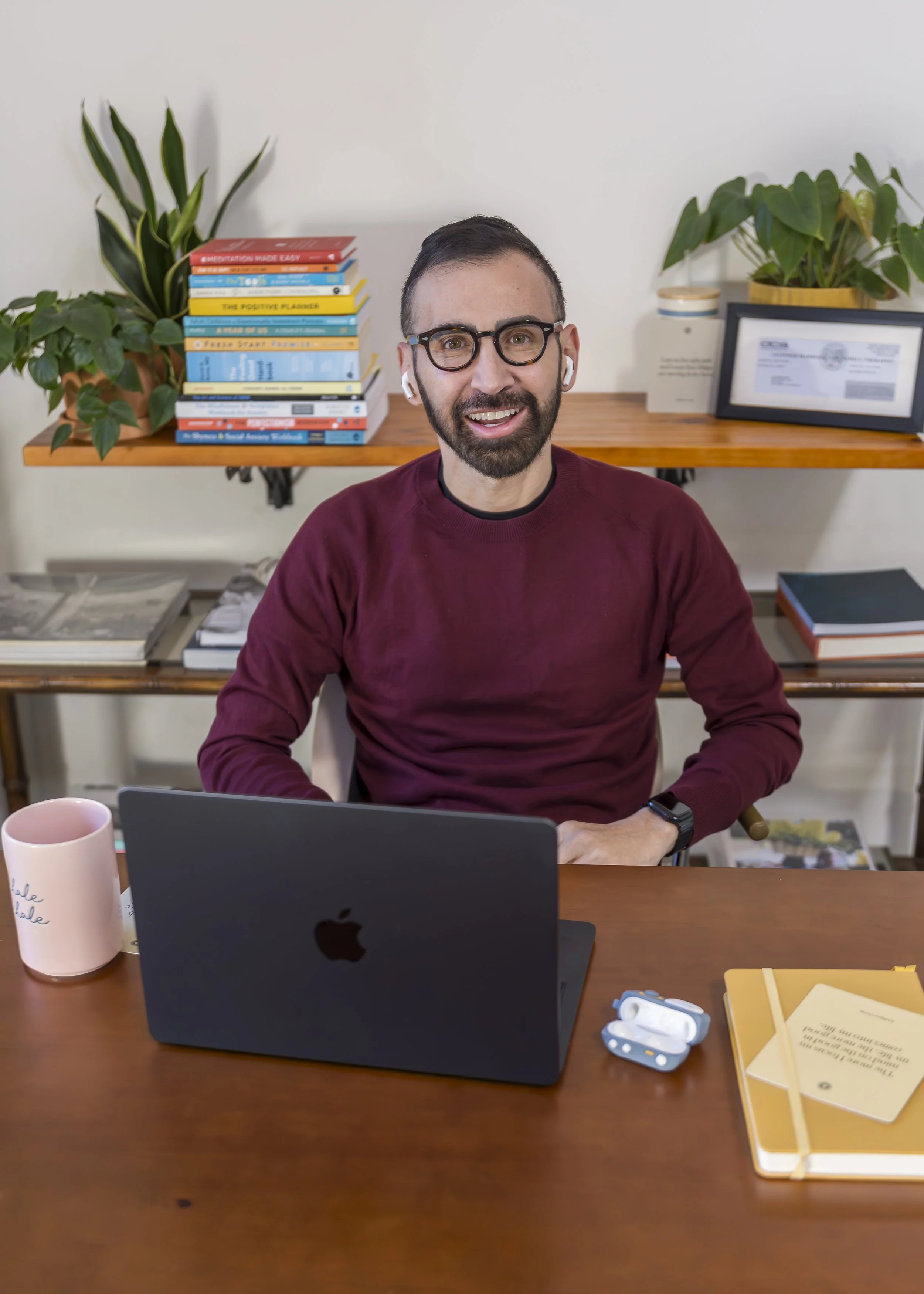 Alex Barragan, LGBTQ-affirming therapist in Los Angeles, smiling at his Westwood office desk