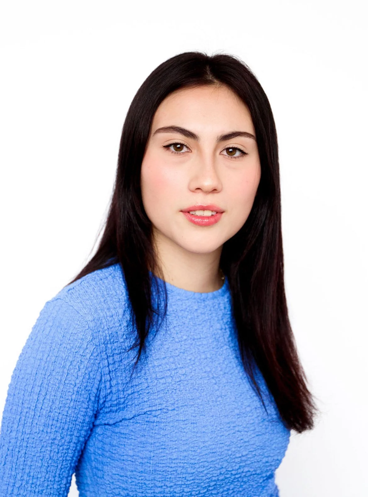 Portrait of a young woman with dark hair wearing a blue textured top, set against a white background.