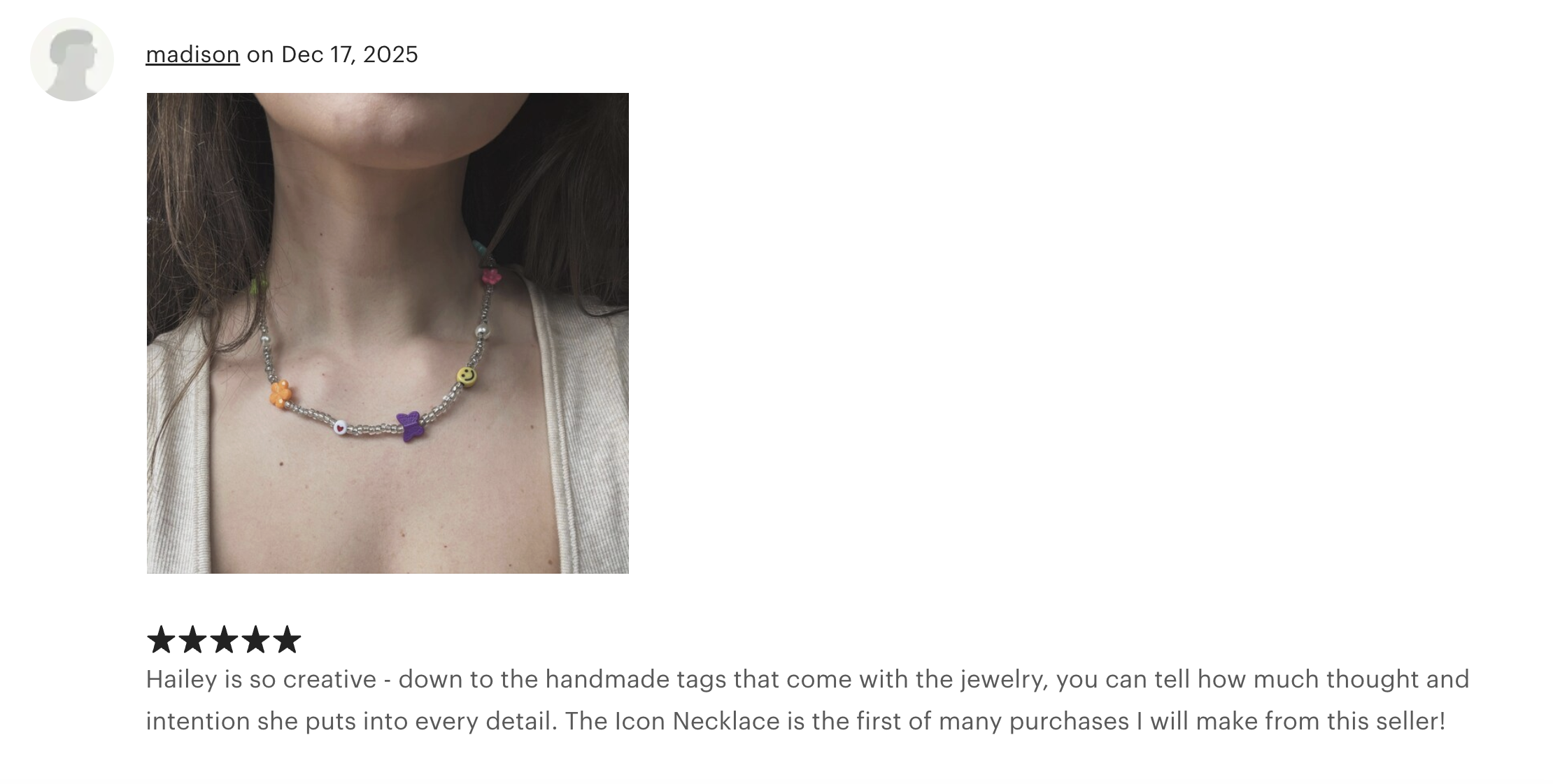 Close-up of a woman's neck and collarbone wearing a colorful beaded necklace with various charms including a purple bow, smiley face, butterfly, and flower.