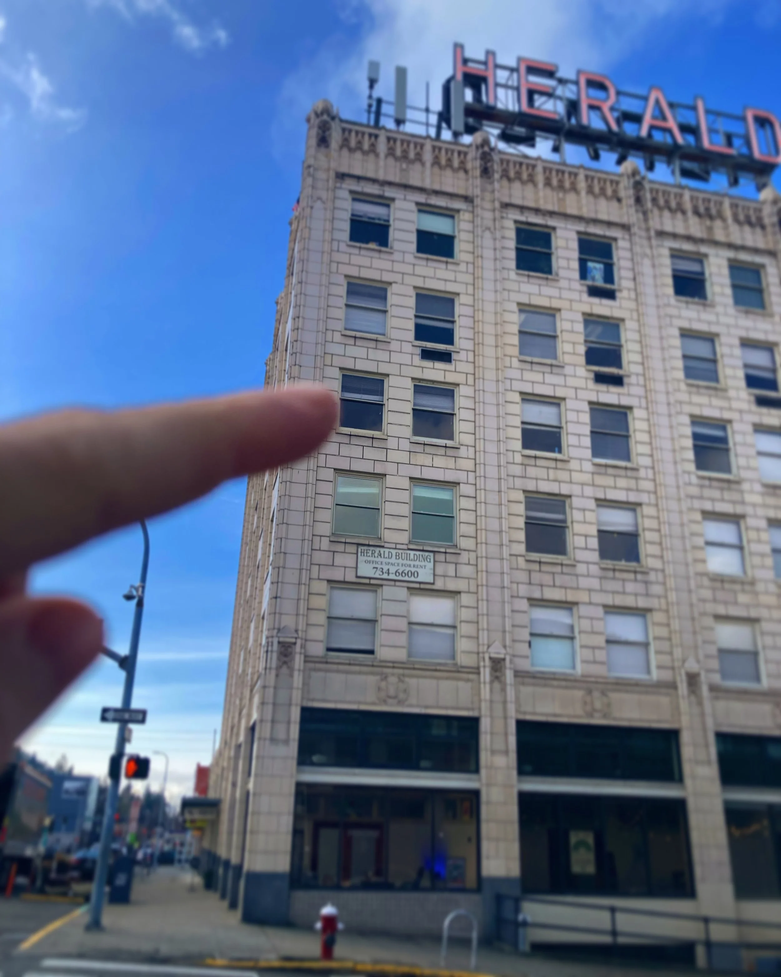 Tall beige building with multiple windows, a sign that reads "HERALD BUILDING OFFICE SPACE FOR RENT 734-6600," and a large red illuminated sign on top that says "HERALD" with part of the sign cut off at the top of the image.