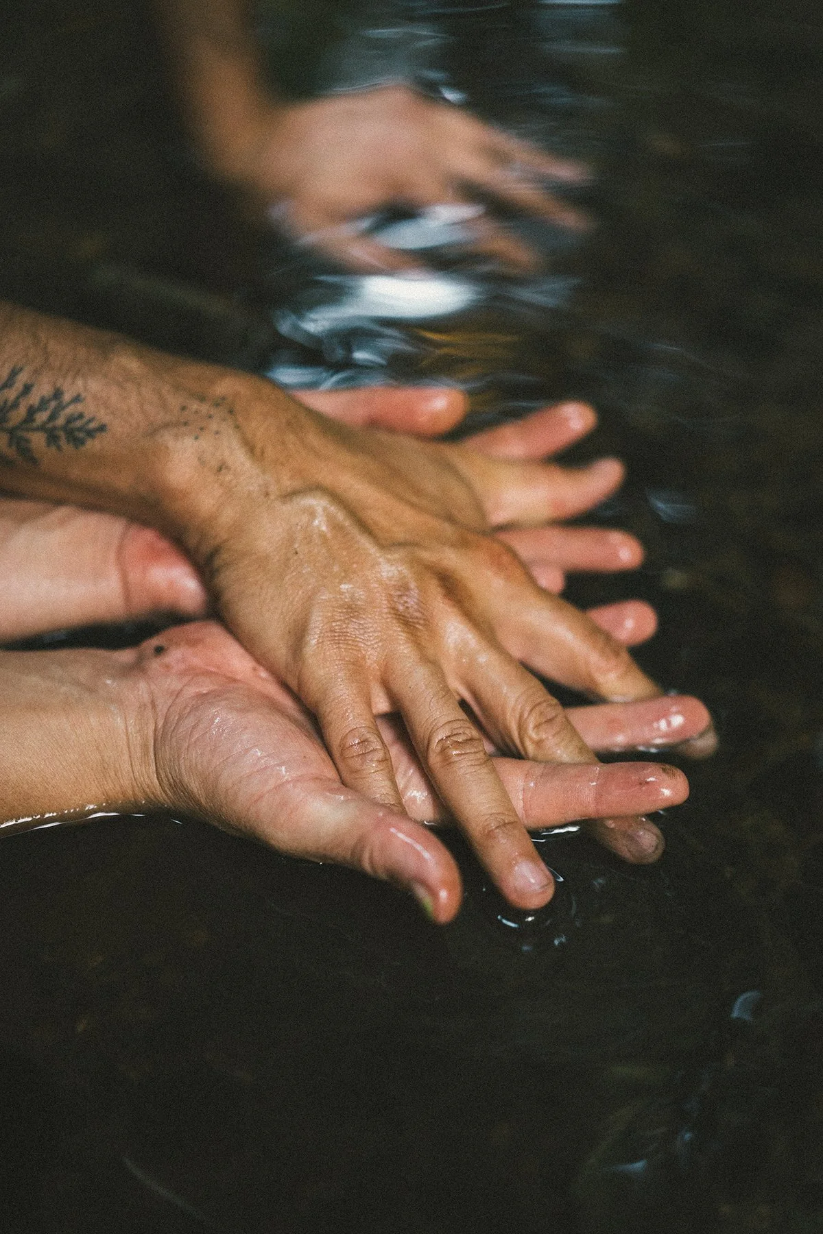 Multiple hands, some with tattoos, touching and holding each other underwater.