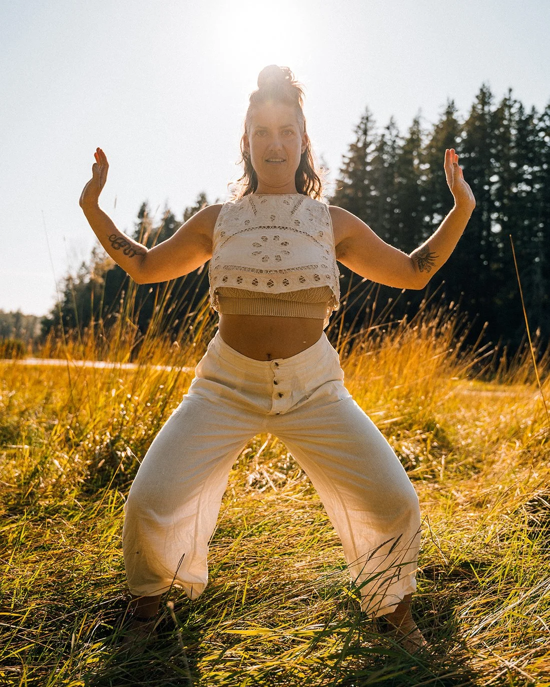 A woman practicing yoga outdoors in a field of tall grass with trees in the background during sunset.