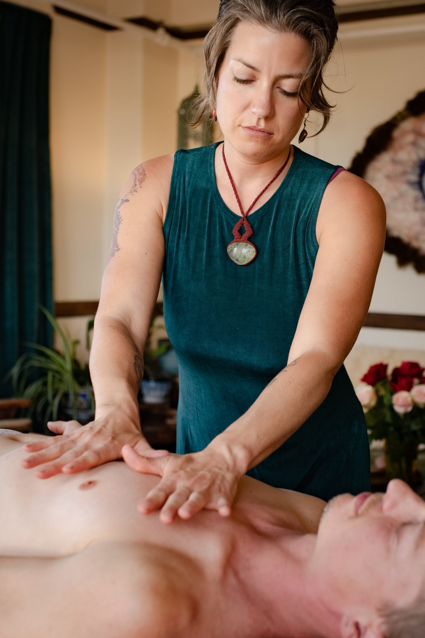 Woman in teal dress giving a massage to a shirtless man lying face up on a massage table.